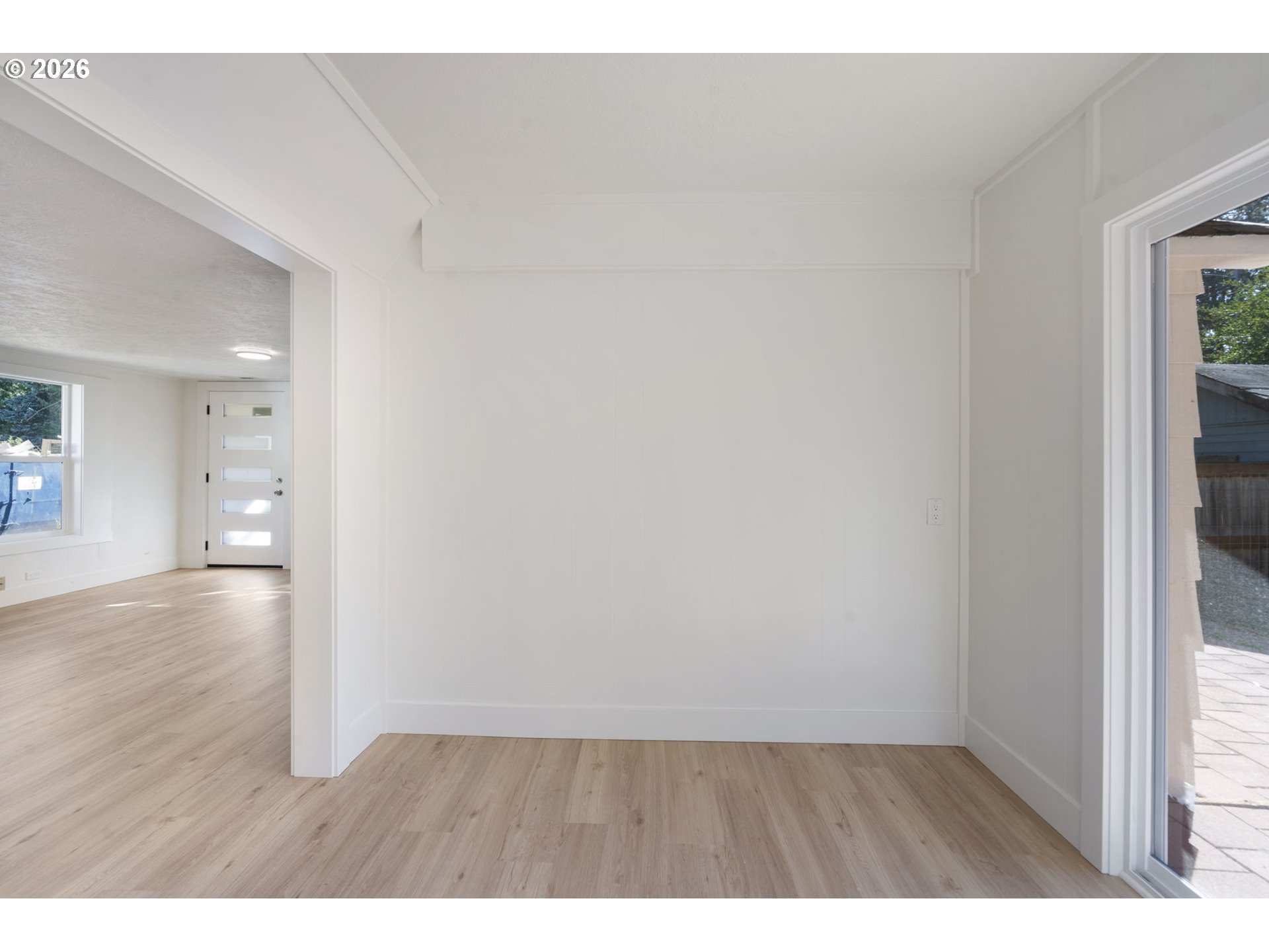 Vacant room with light wood floors, white paneled walls, and a glass door to the patio.