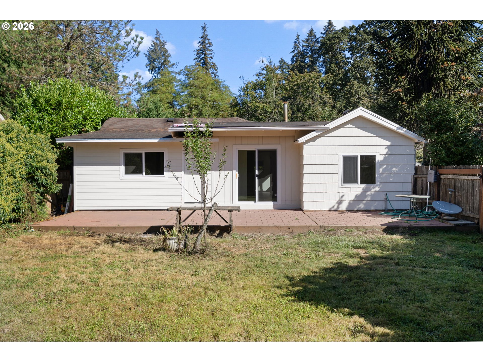 Rear of a white single-story house with a broad brick patio deck and fenced backyard.