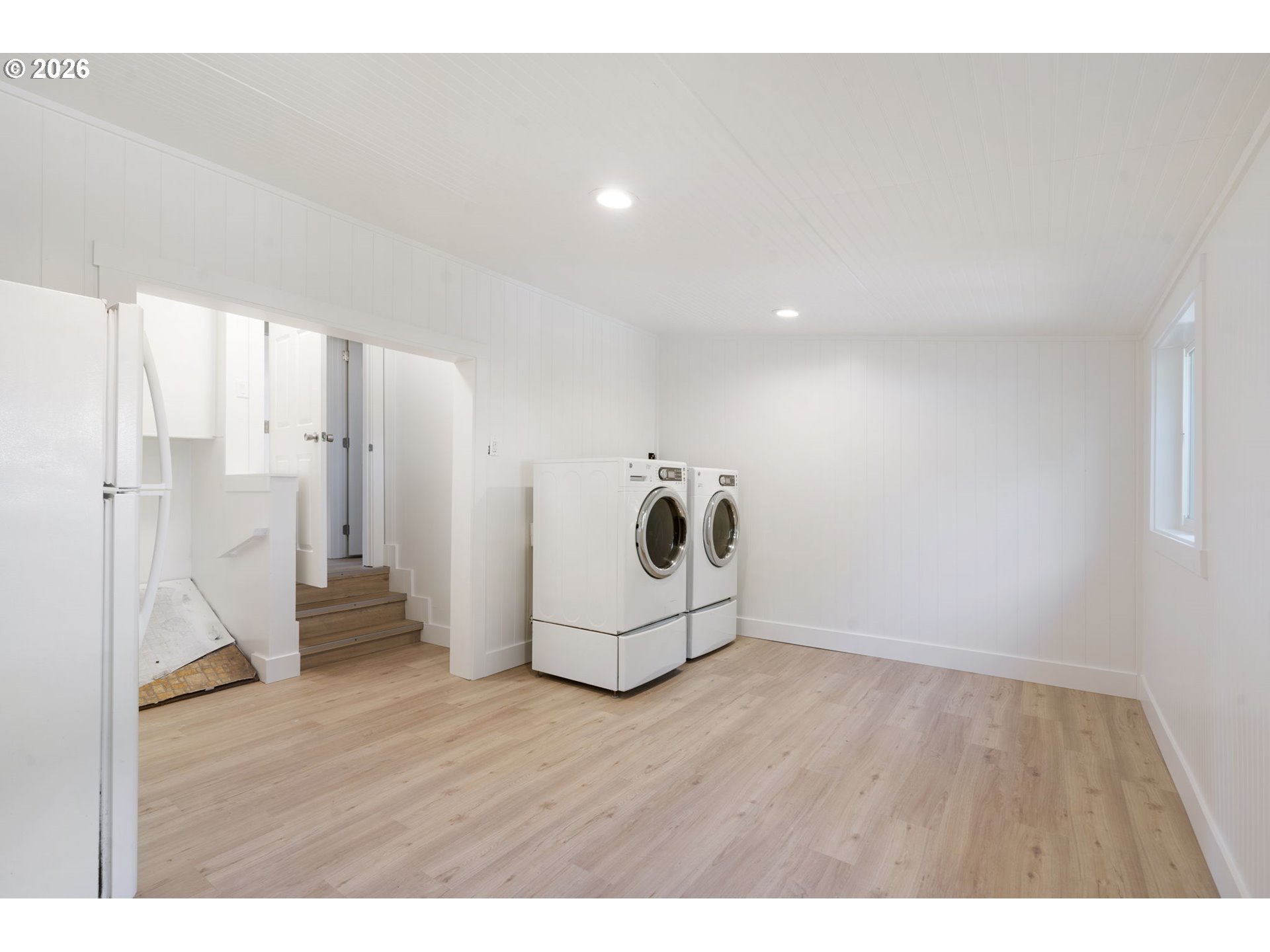 Laundry room with front-loading washer and dryer, refrigerator, and light wood-look flooring.