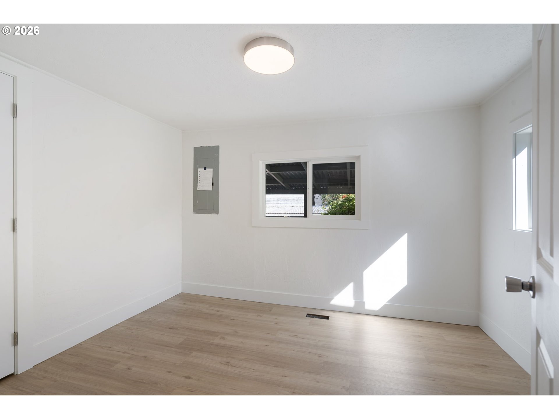 Empty room with light wood-look flooring, a low window, and an electrical panel.