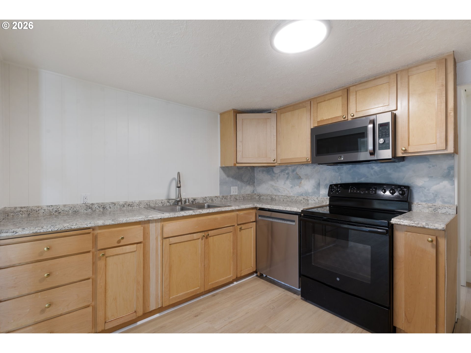 Kitchen with light wood cabinets, speckled countertops, and black range and microwave.