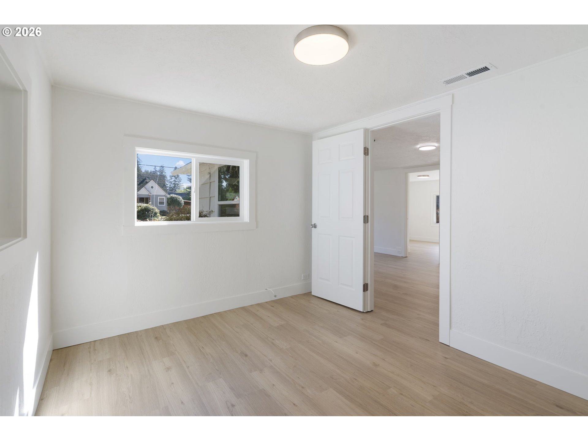Vacant room with pale wood-look flooring, a window, and an open doorway.