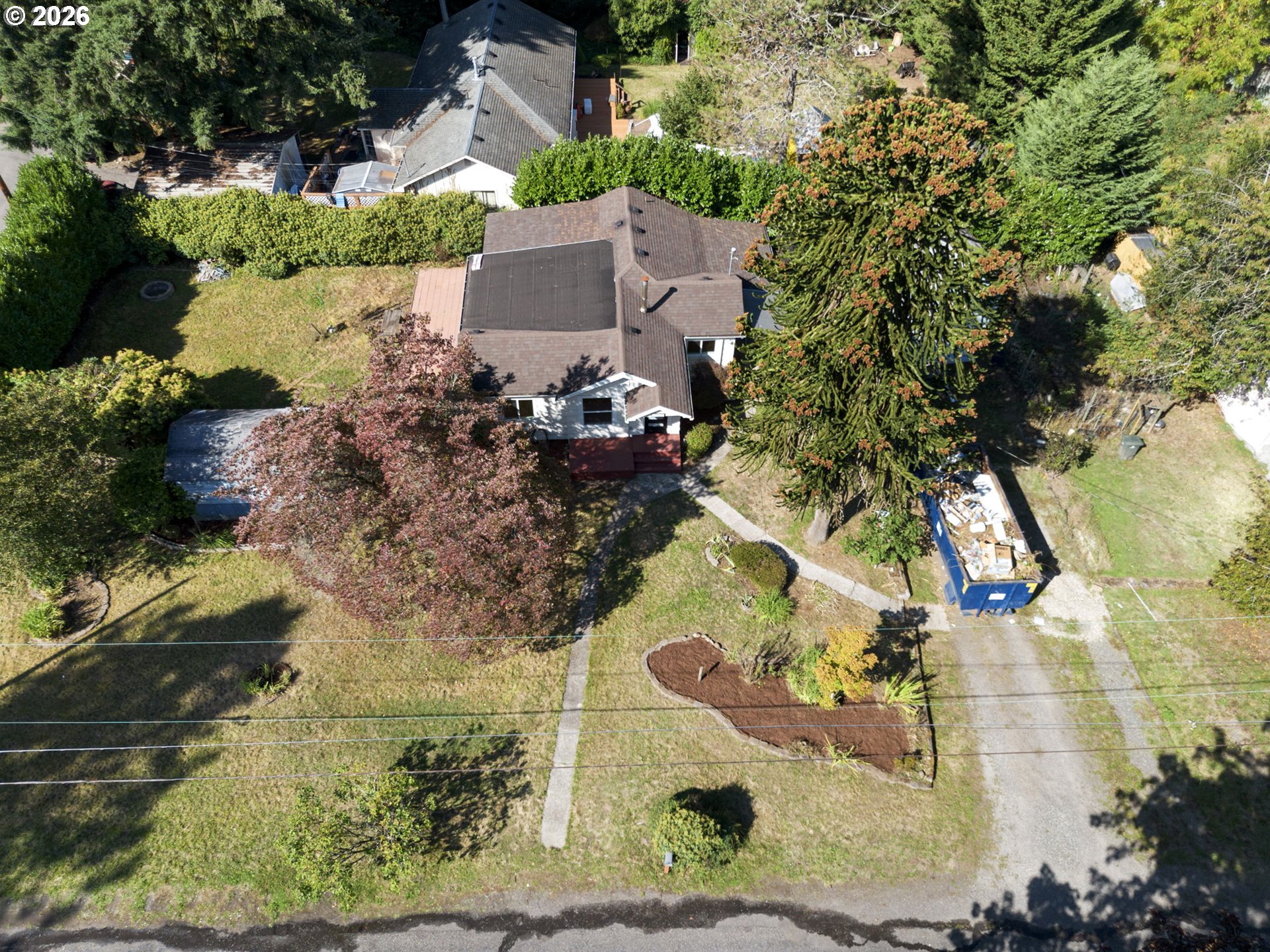 Aerial view of a house with a large yard, mature trees, and a driveway.
