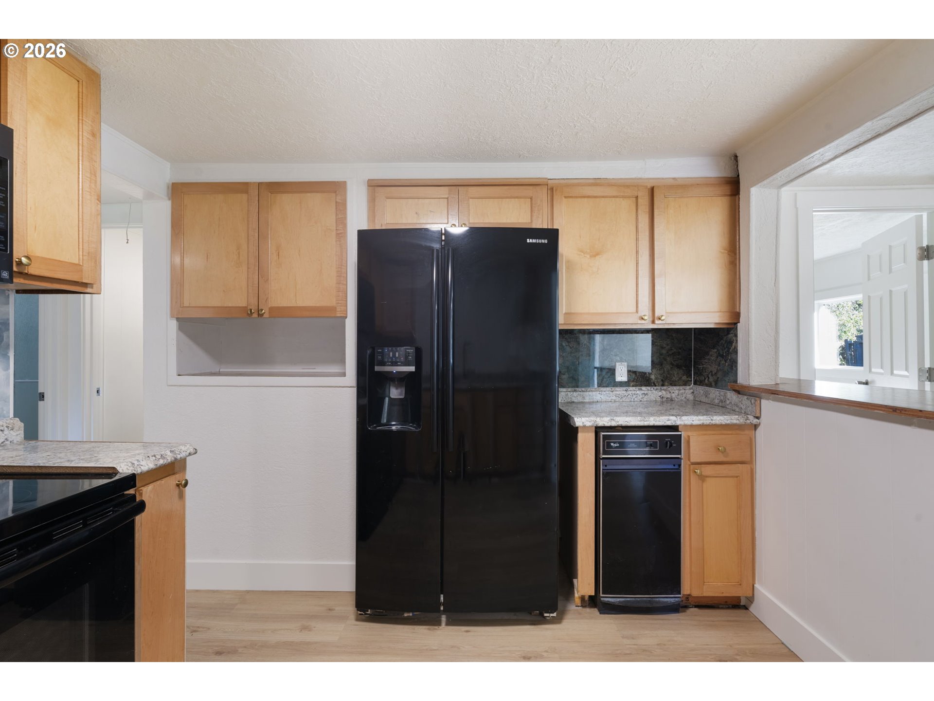 Kitchen with light wood cabinets, granite counters, and a black side-by-side refrigerator.