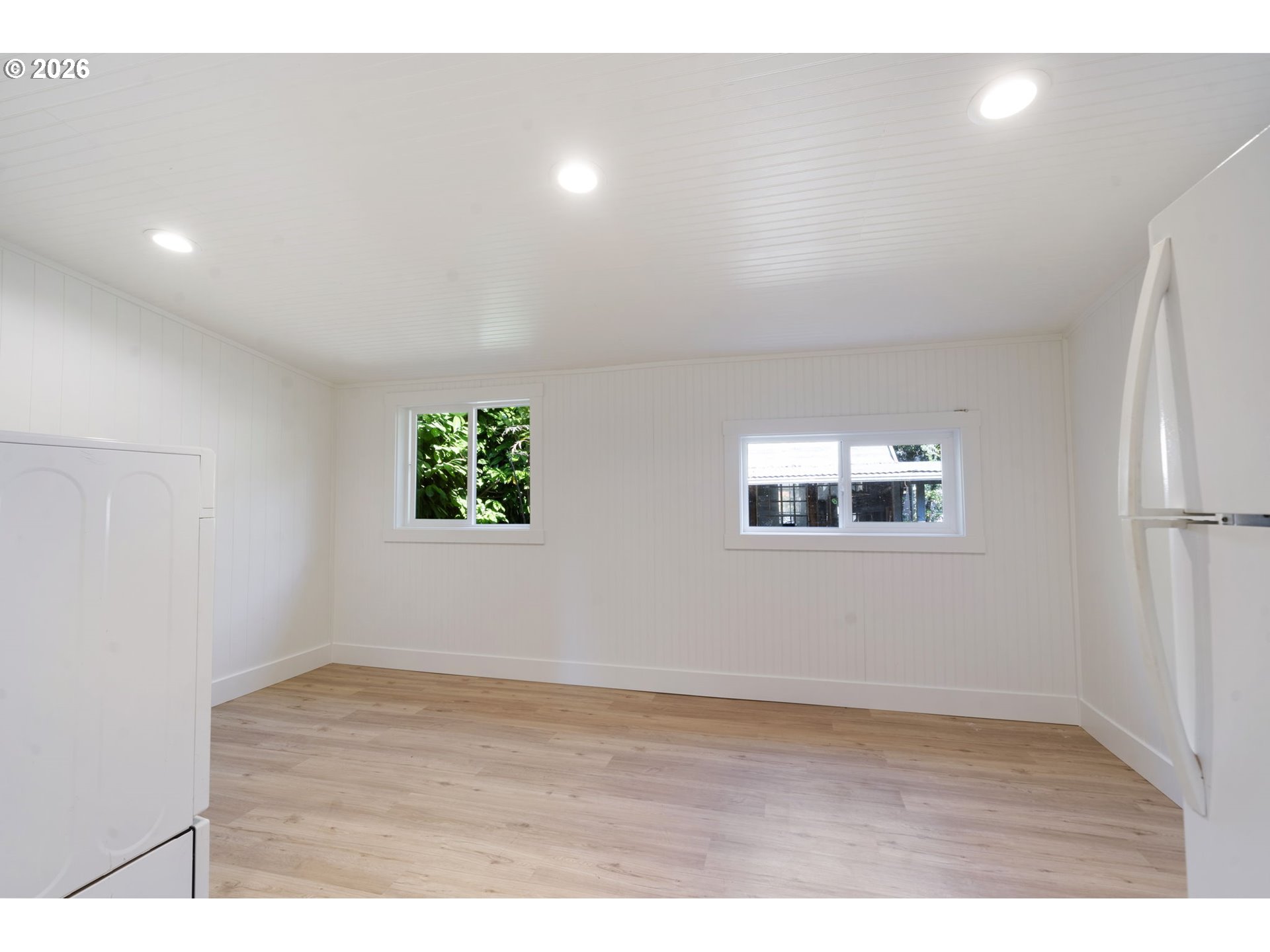 Vacant white-paneled room with wood-look flooring, two windows, and a wall-mounted fold-down fixture.