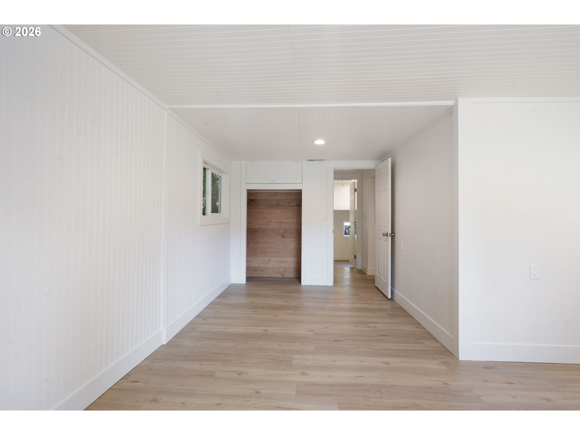 Empty room with light wood floors, white paneling, and a wood-backed closet nook.