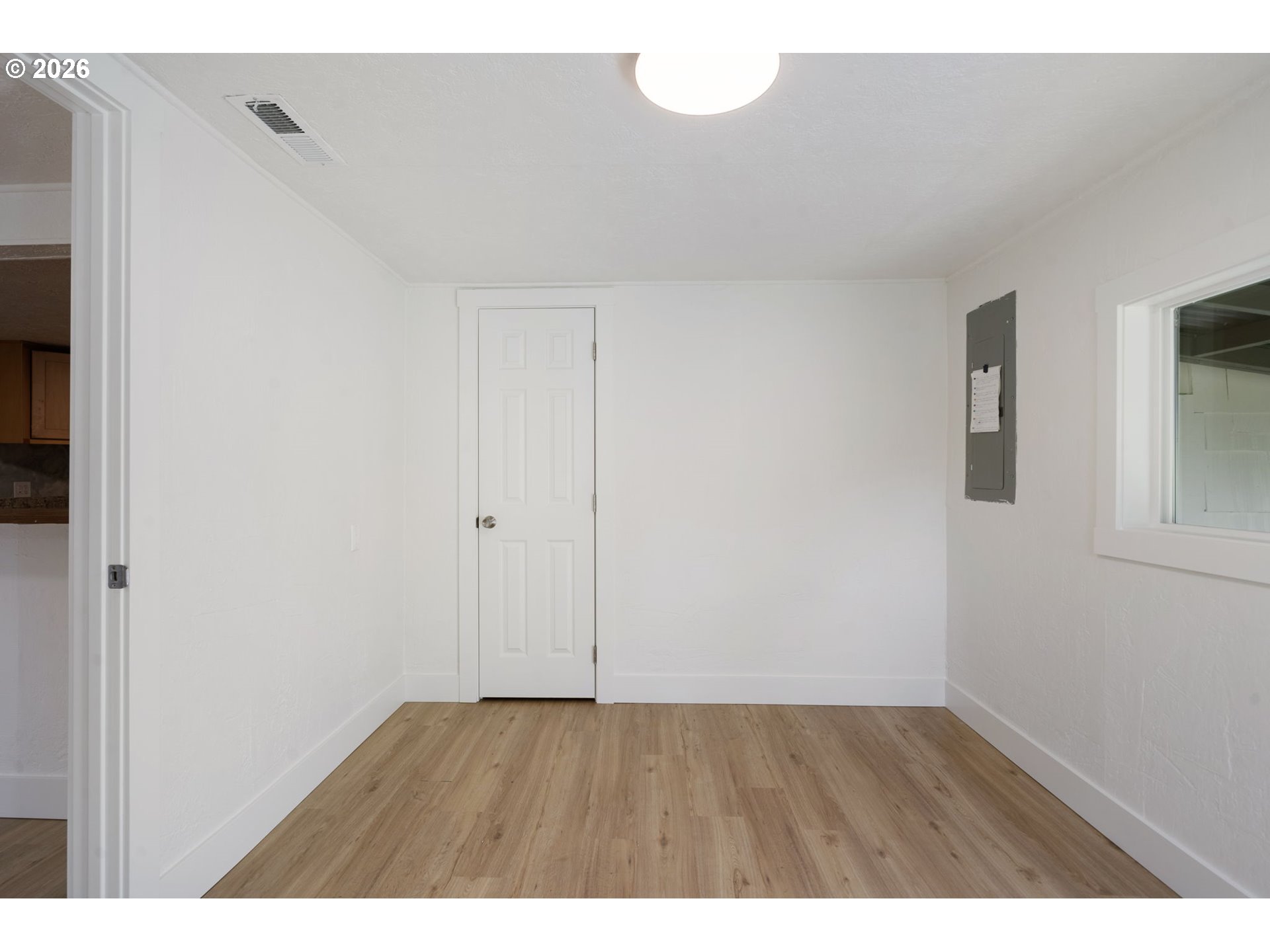 Vacant room with light wood-look flooring, a white paneled door, and a wall-mounted electrical panel.