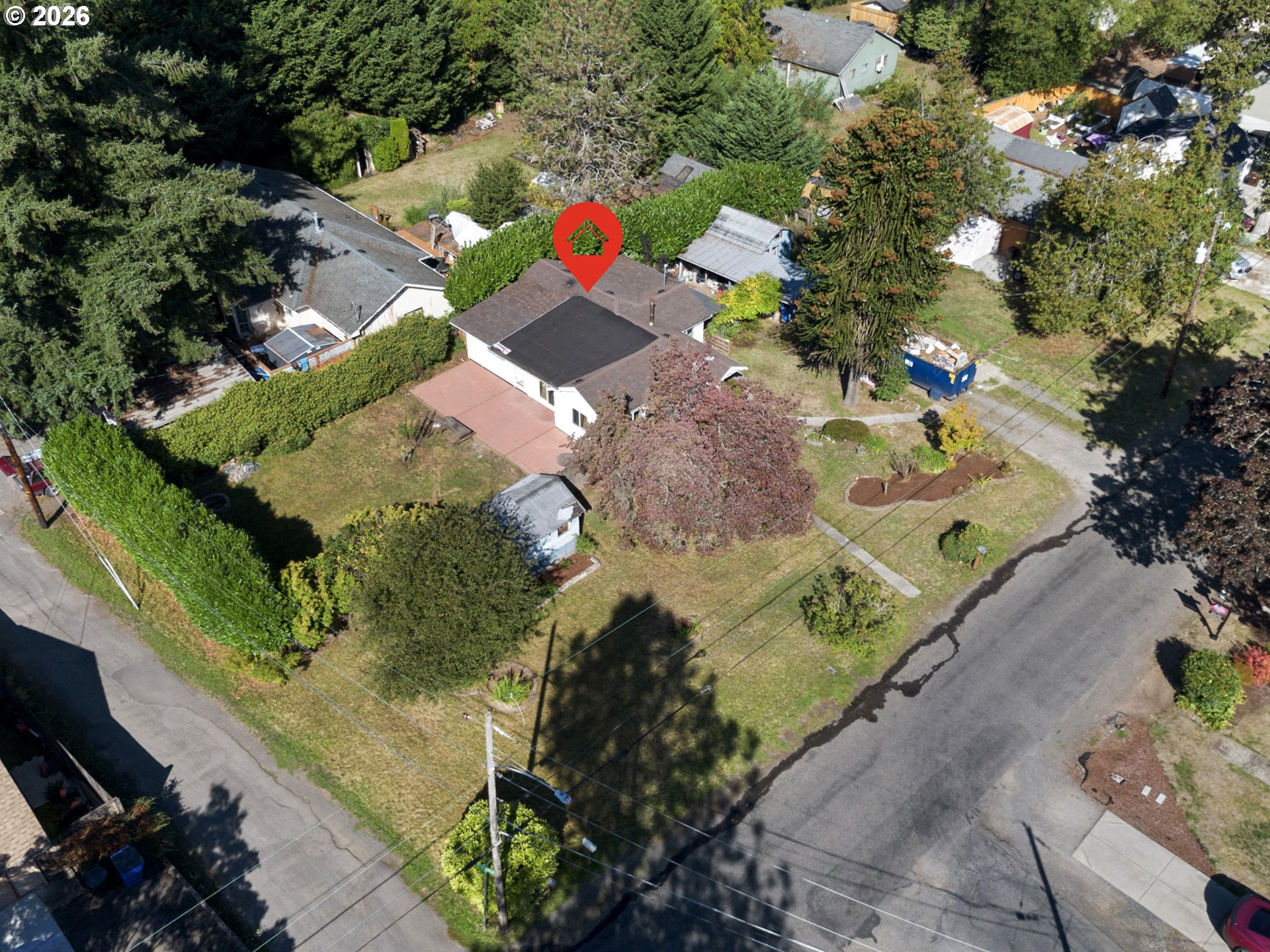 Aerial view of a single-story home on a leafy corner lot with a hedged yard and patio.