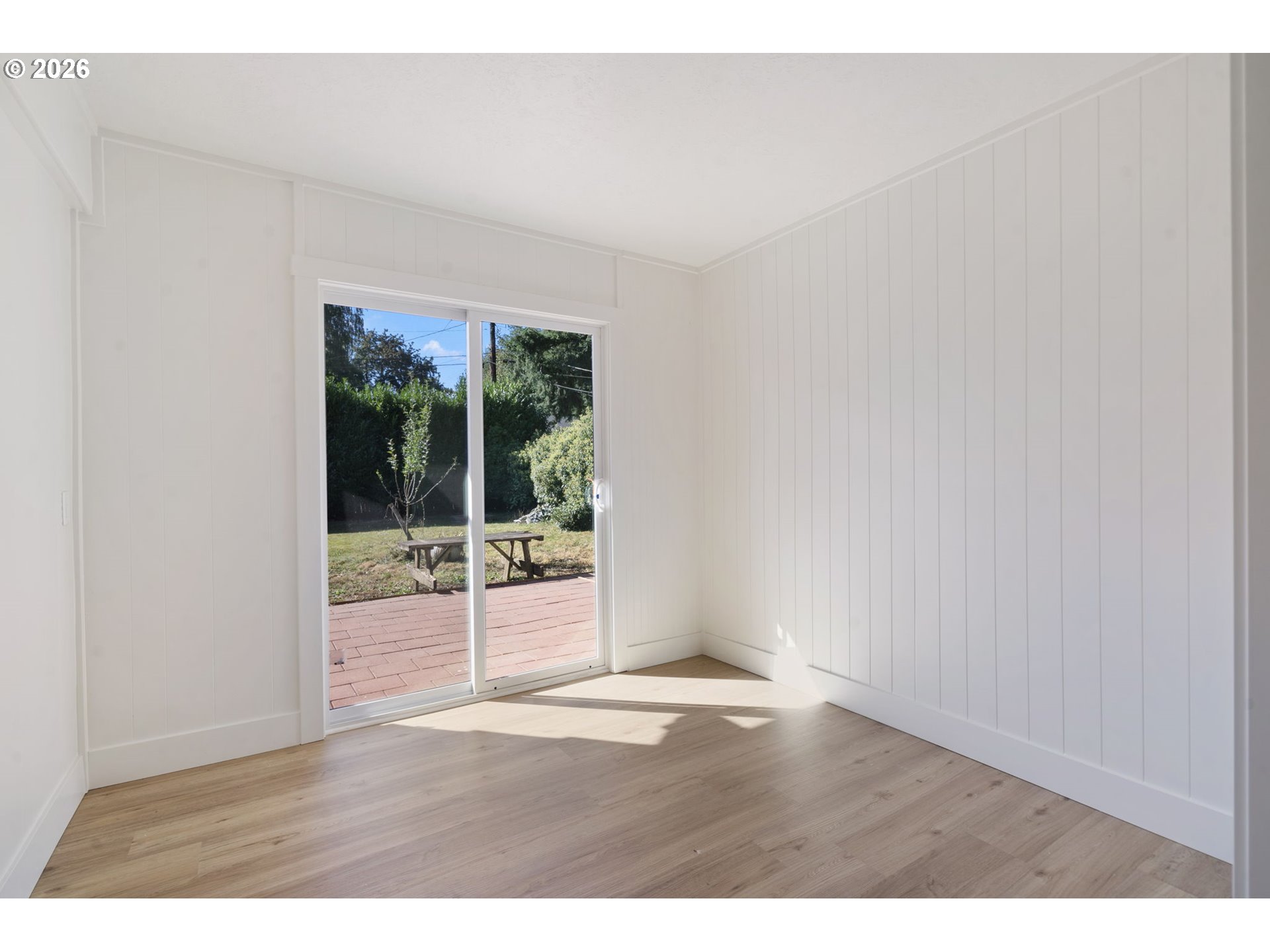 Empty room with light wood floors and a sliding glass door opening onto a brick patio.