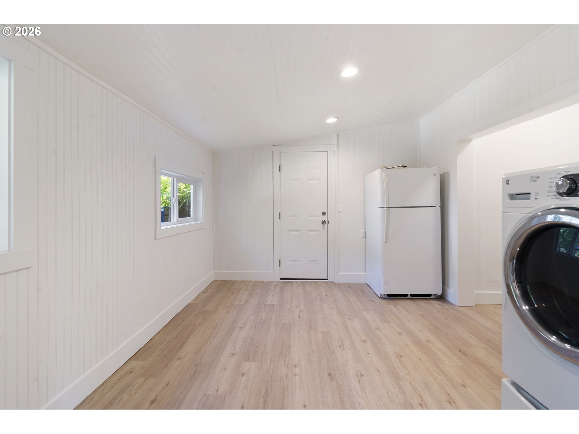 Laundry room with a refrigerator, front-loading washer and dryer, and light wood-look flooring.