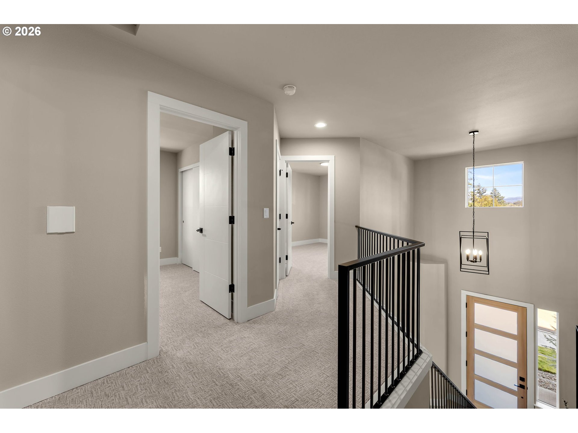 Upstairs hallway landing with light carpeting, open doors, and a black metal stair railing.