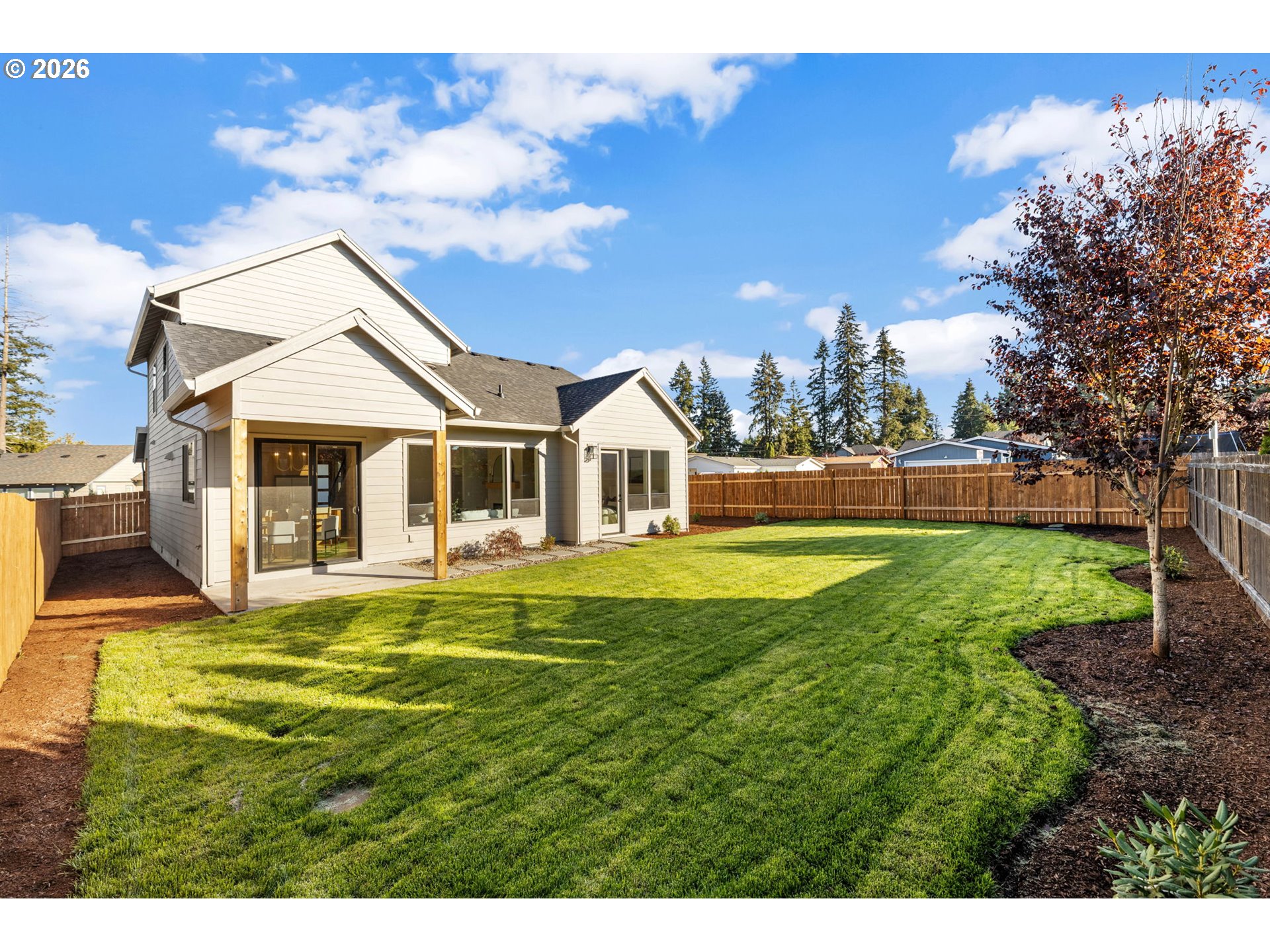 Home’s rear exterior and covered patio overlook a broad, fenced lawn with a mature autumn tree.