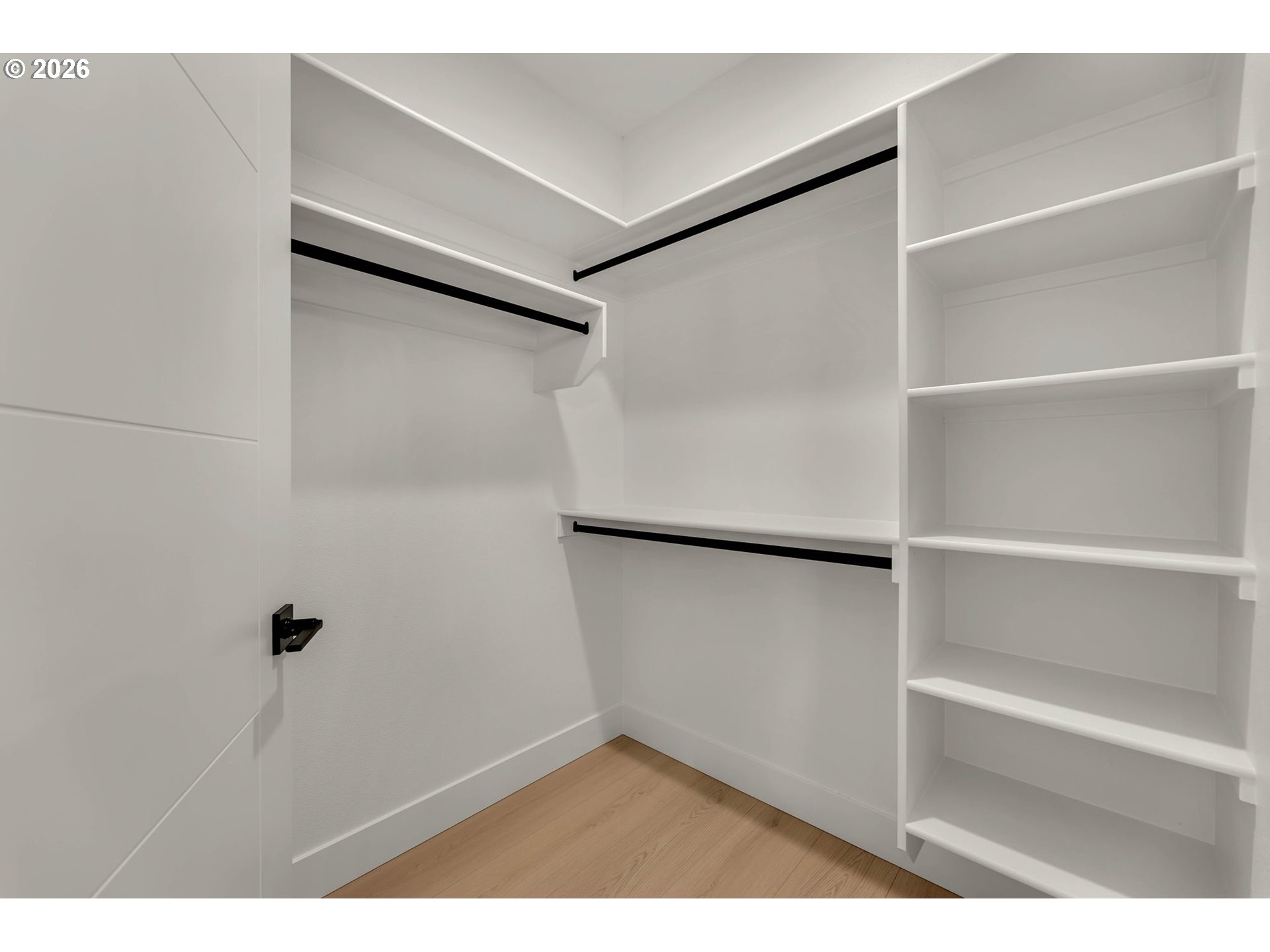 Walk-in closet with white built-in shelves, black hanging rods, and light wood flooring.