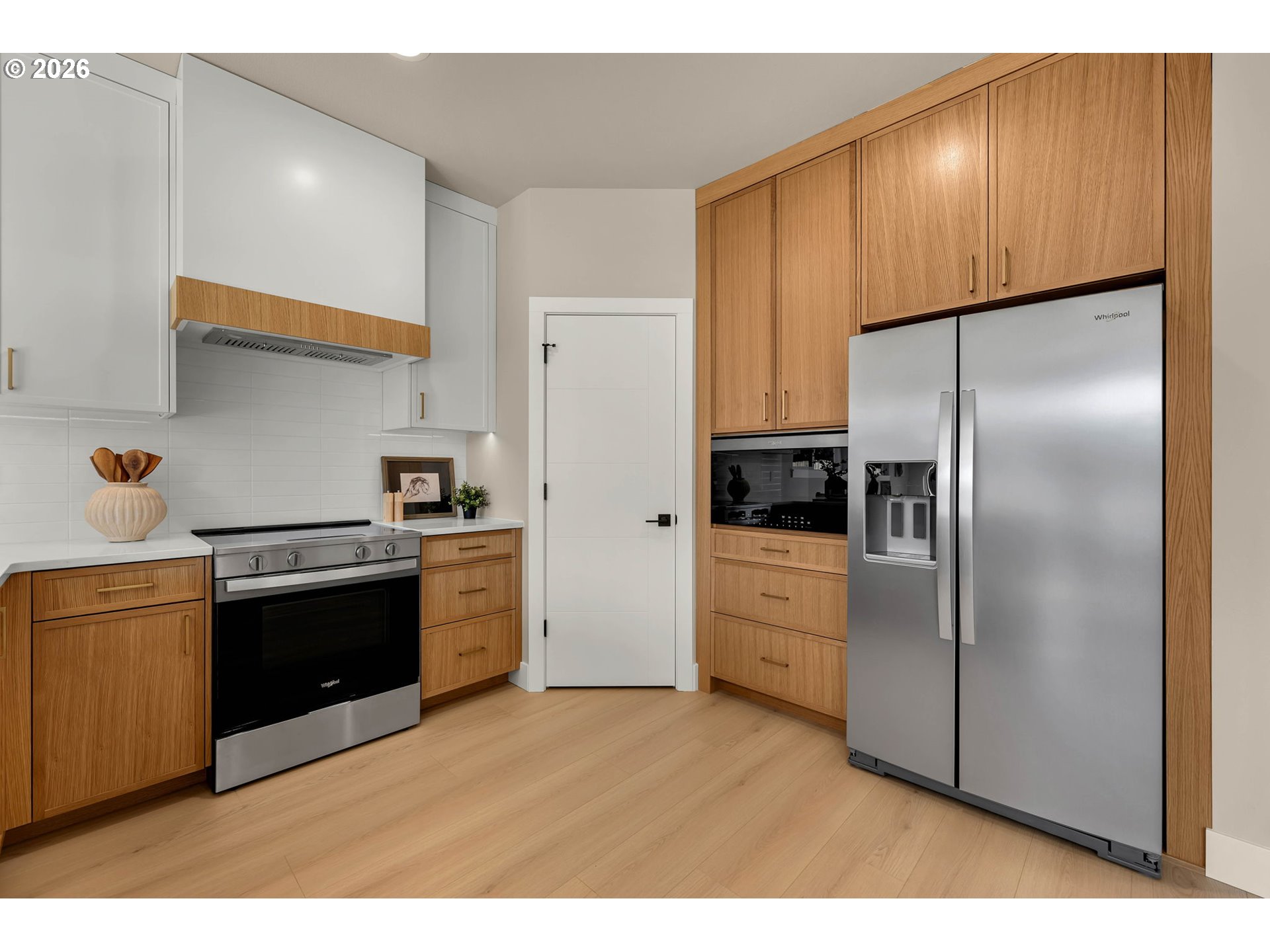 Modern kitchen with warm wood cabinets, stainless steel appliances, and light wood flooring.