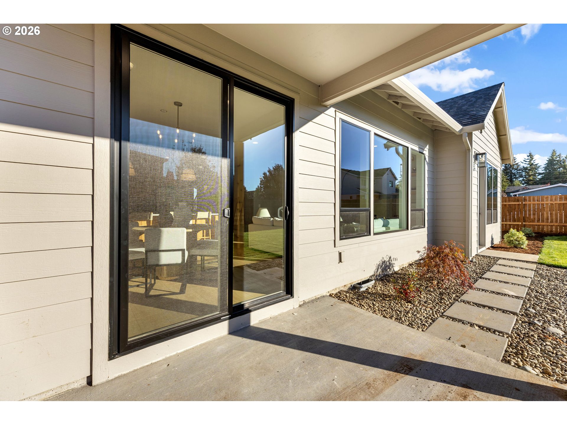 Rear patio with a black-framed sliding glass door and stepping stones beside a stone garden bed.