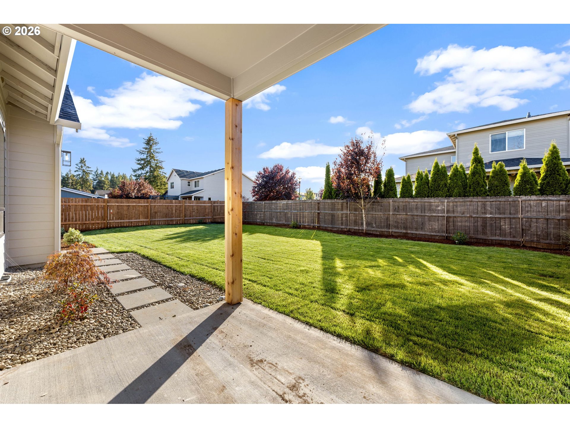 Covered patio overlooking a fenced lawn with a stepping-stone path and rock garden.