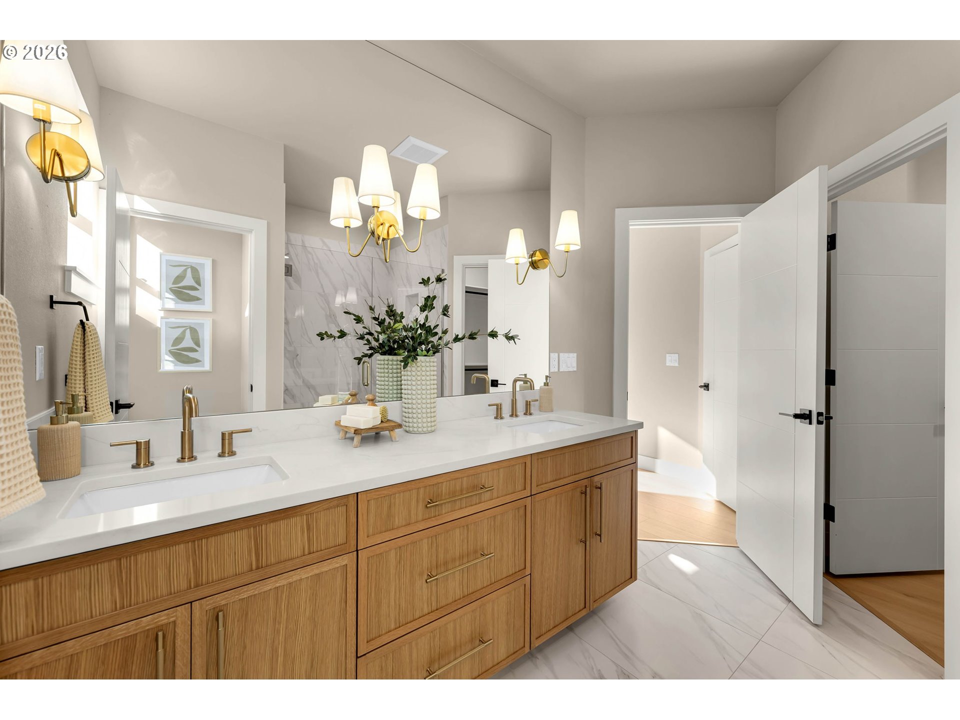 Bathroom with a long double vanity, warm wood cabinets, brass fixtures, and marble-look tile.