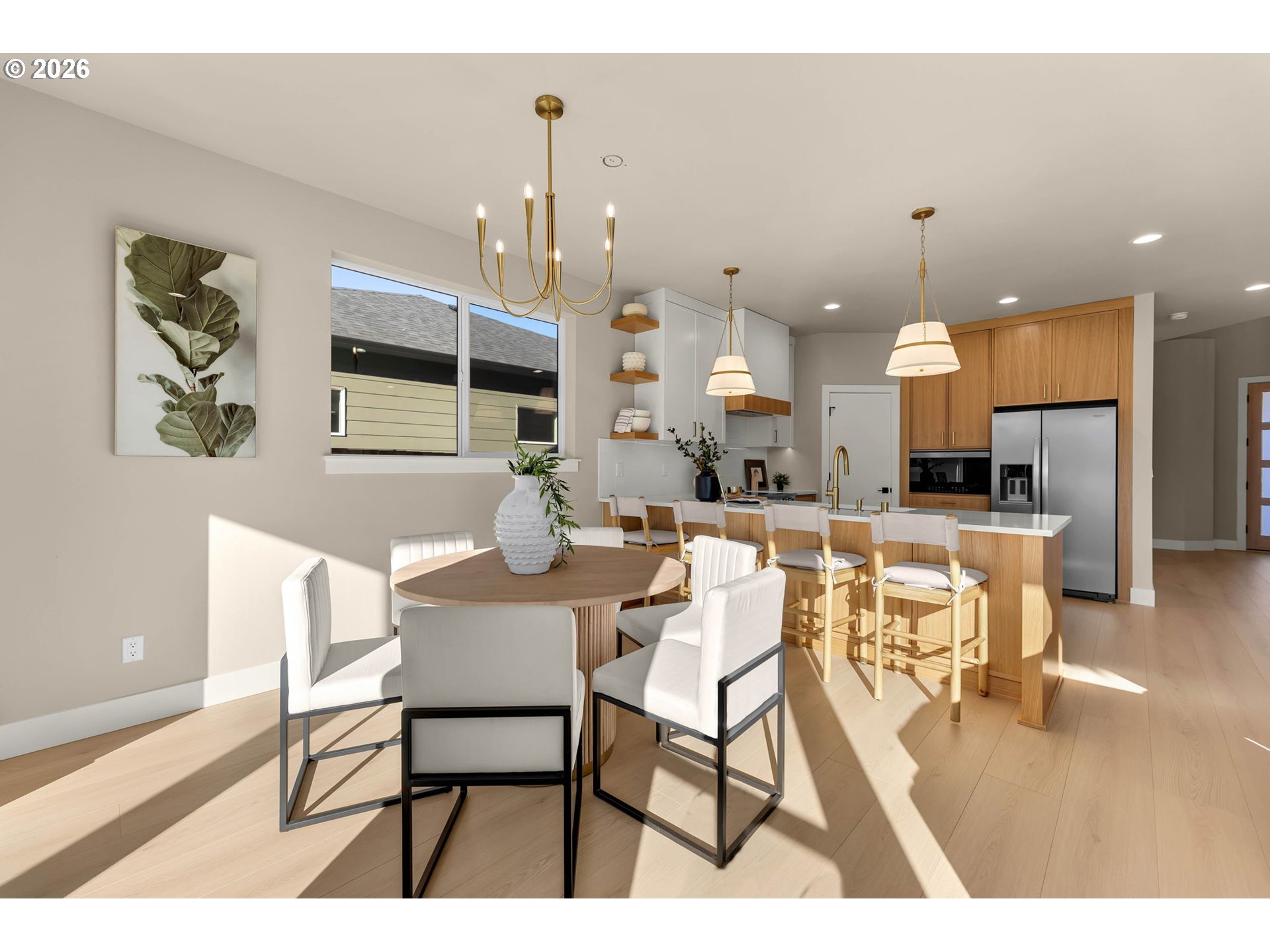 Open-plan kitchen and dining area with a round table, wood island, and sunlit pale floors.