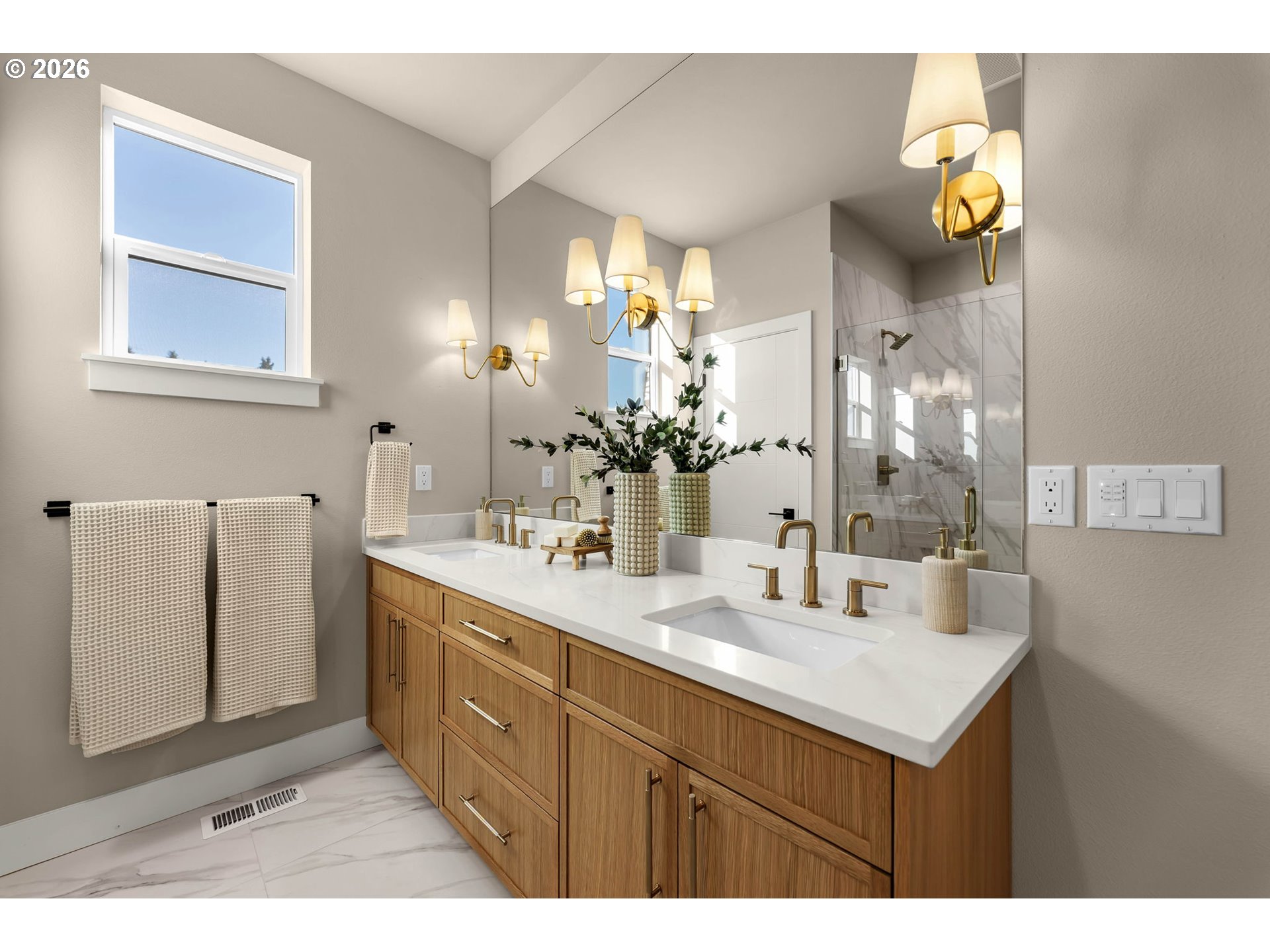 Bathroom with a double-sink wood vanity, brass fixtures, and a marble-look tiled shower.