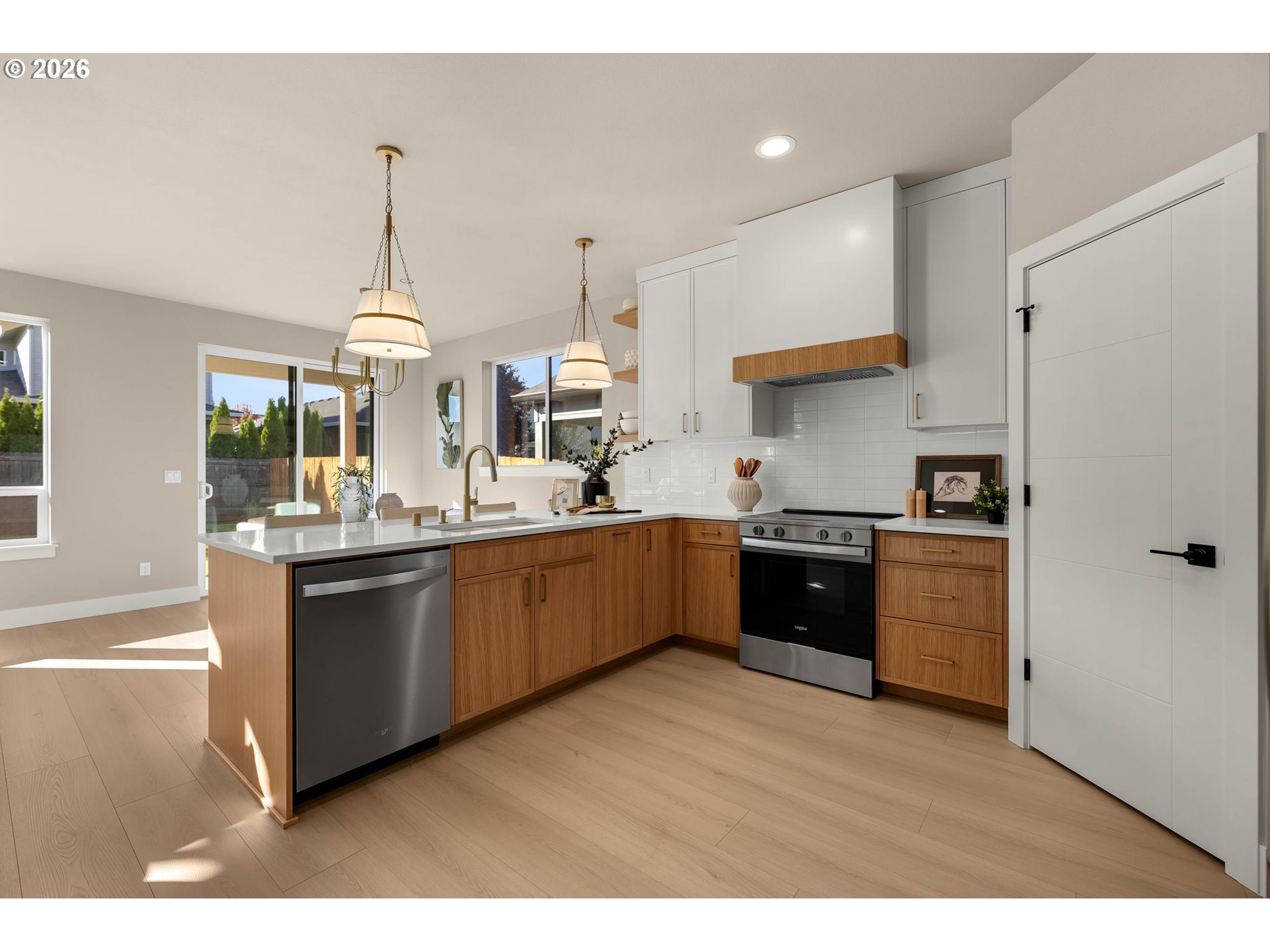 Modern kitchen with warm wood cabinets, a white island, stainless appliances, and pendant lights.