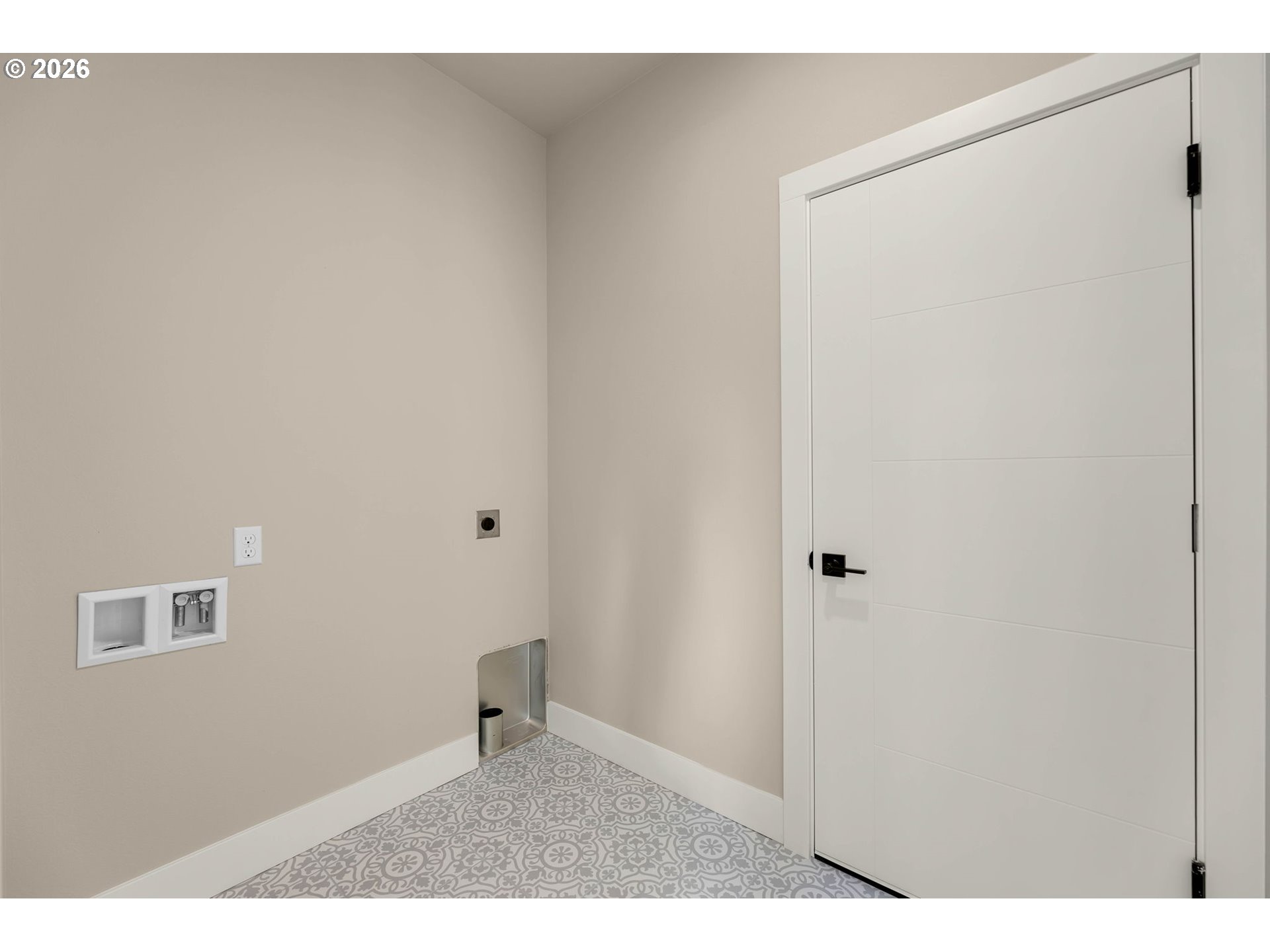 Laundry area with washer hookups, patterned tile flooring, and a white door.