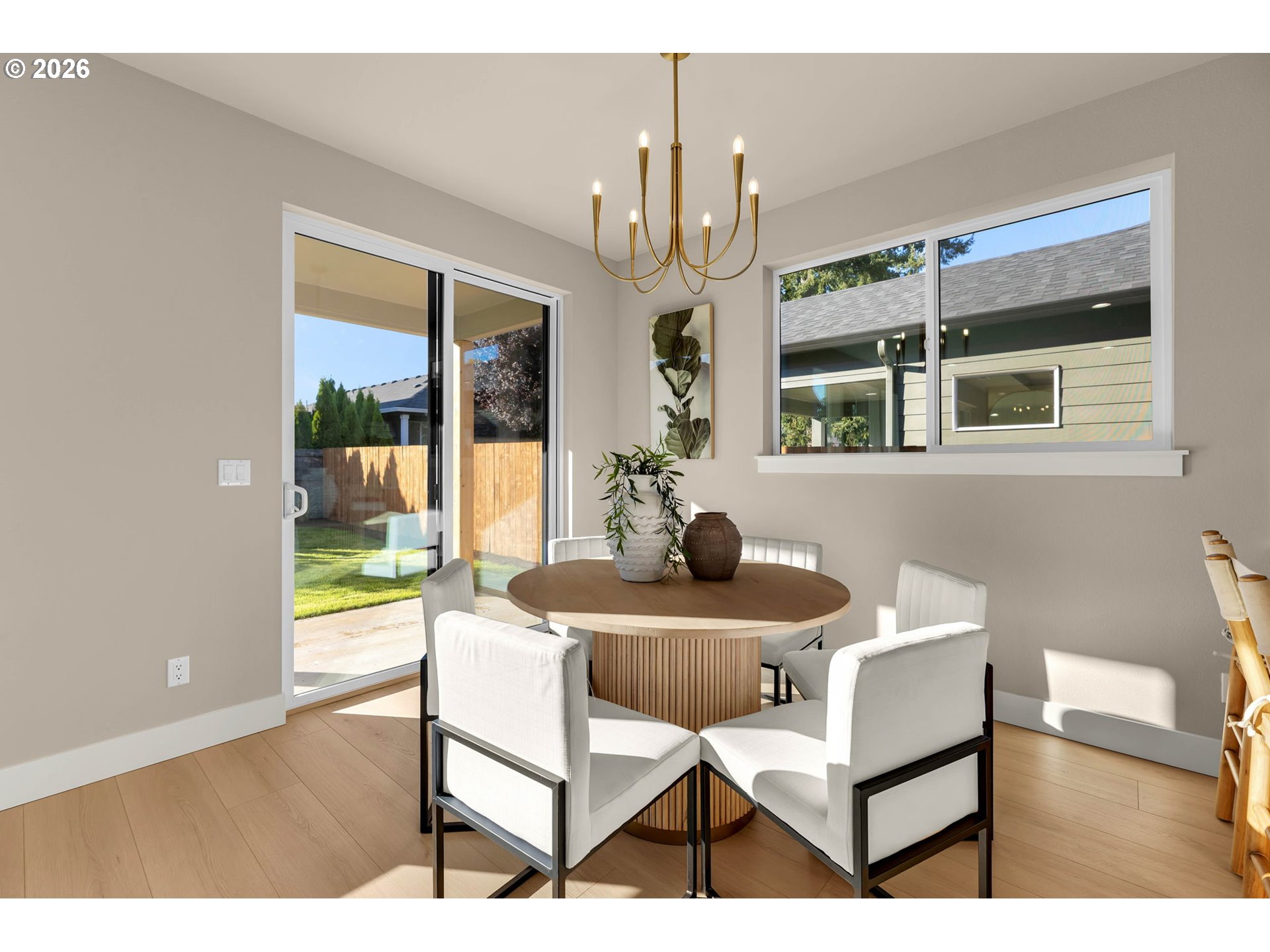 Dining room with a round wood table, white chairs, and sliding glass doors to the backyard.