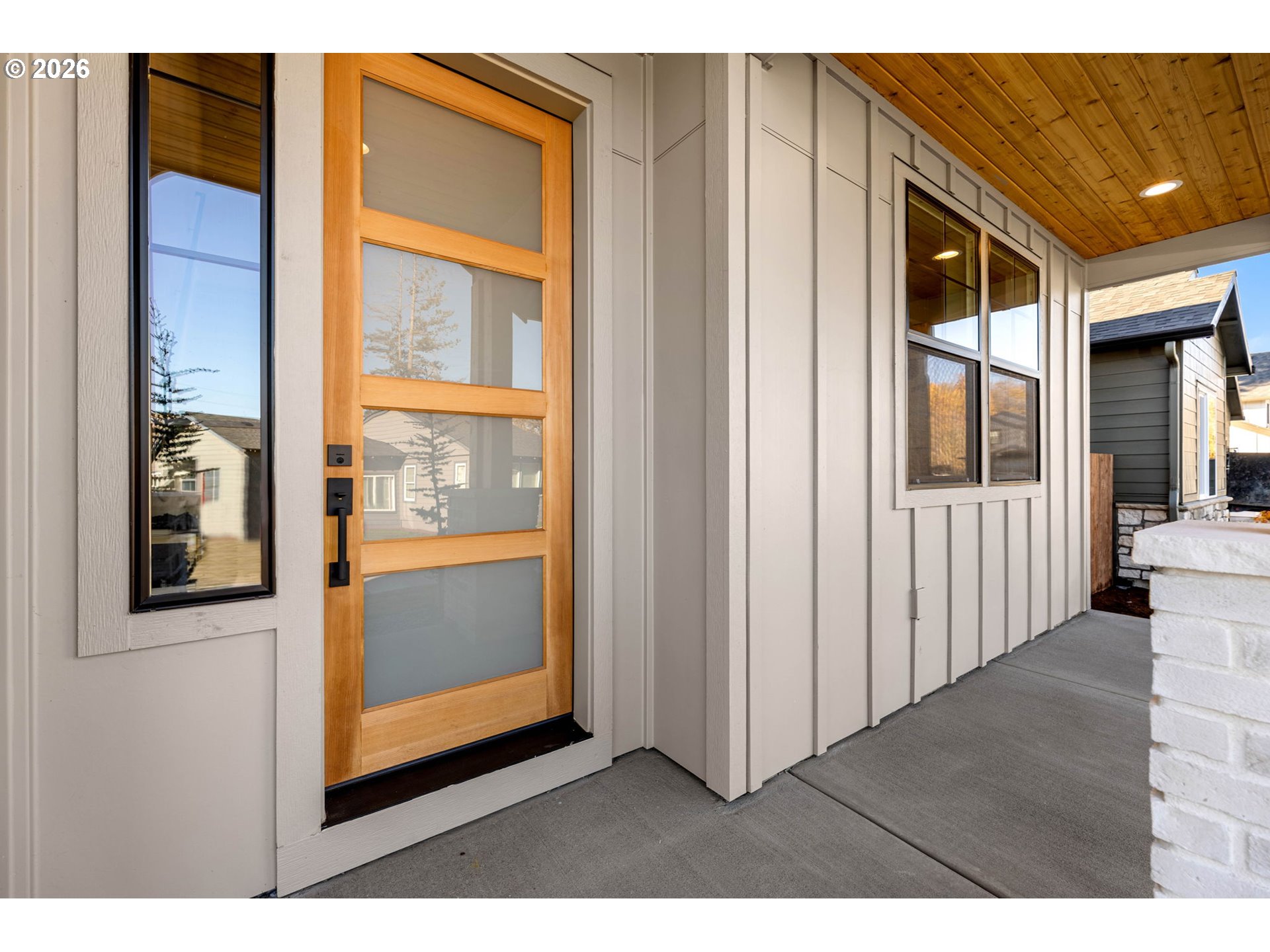 Covered front porch with a wood-framed glass door and warm wood ceiling.