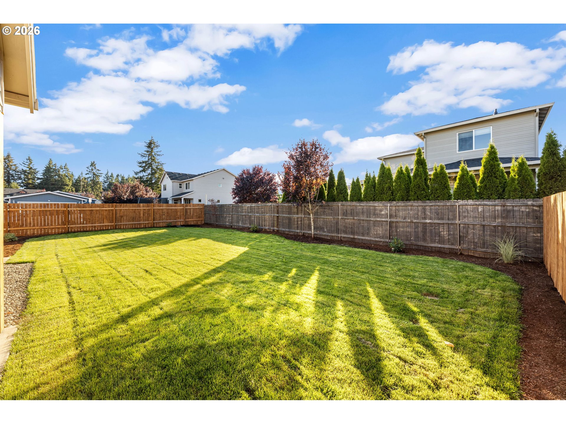 Fenced backyard with a broad green lawn, wooden privacy fences, and landscaped borders.