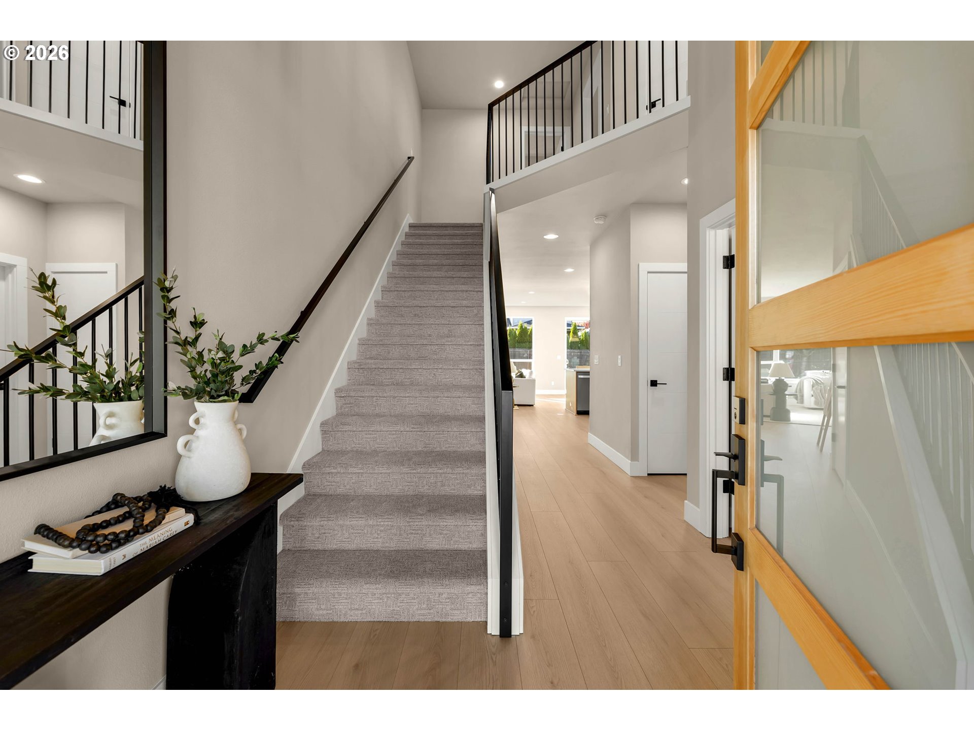 Two-story entryway with a carpeted staircase, black railings, and an open wood-framed glass door.