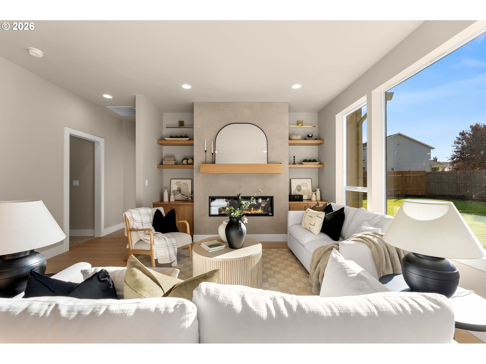 Staged living room with a modern fireplace, built-in wood shelves, and large windows overlooking the backyard.