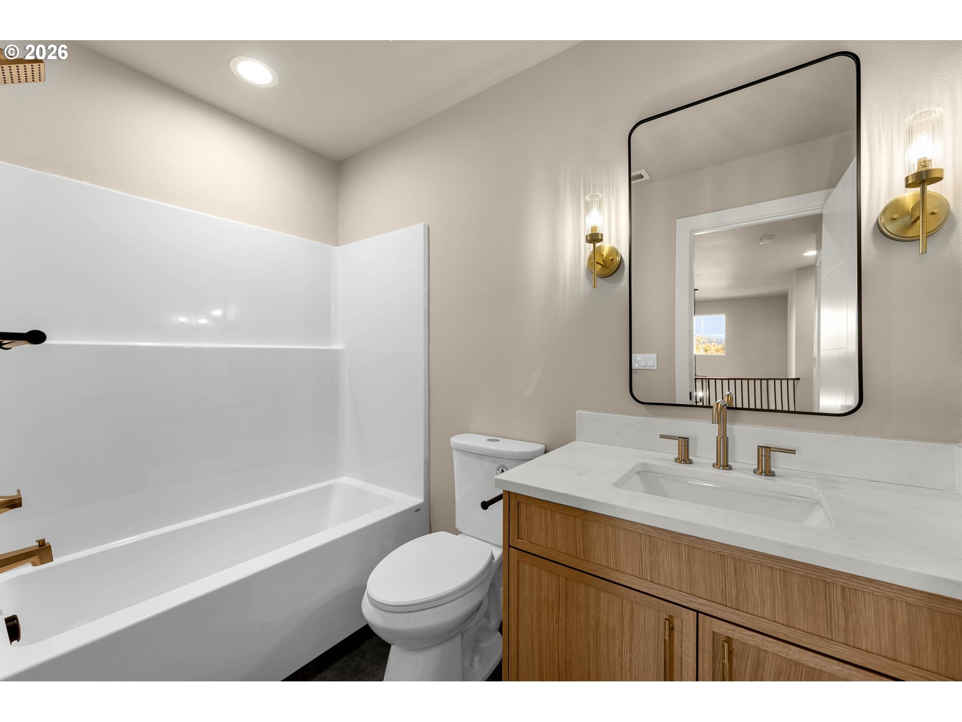 Bathroom with a white bathtub, wood vanity, black-framed mirror, and brass fixtures.
