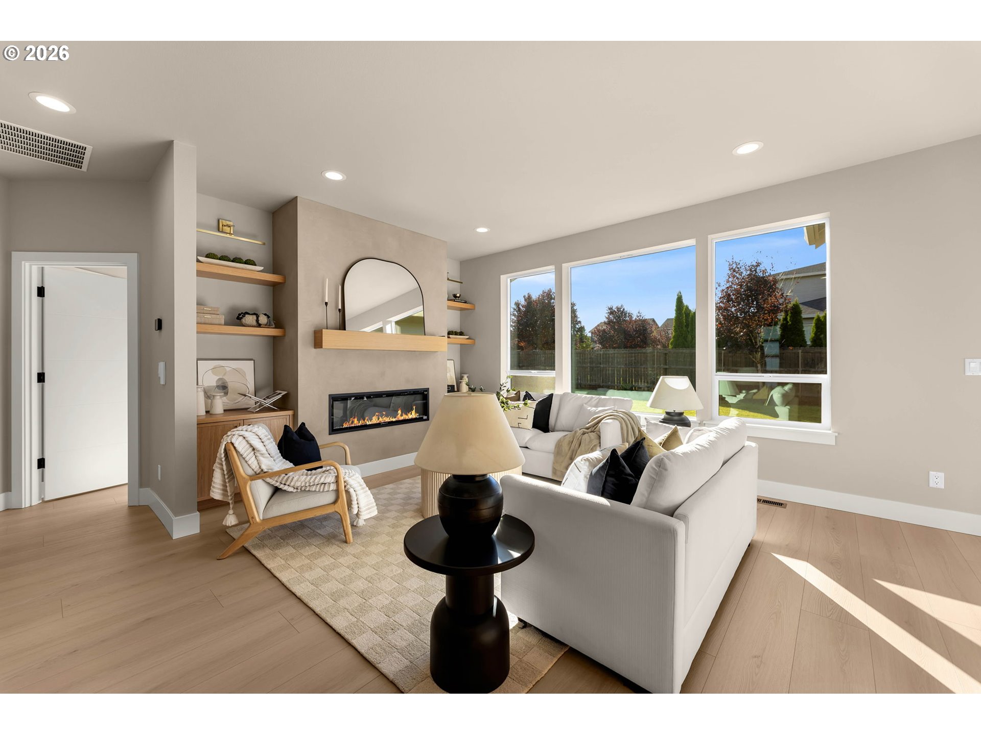 Staged living room with white sofas, built-in shelves, a linear fireplace, and large windows overlooking the backyard.