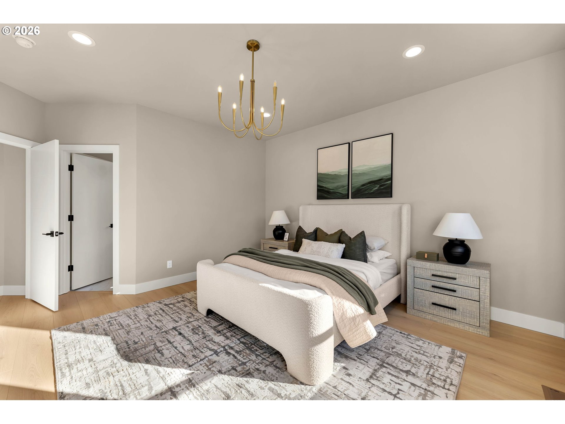 Staged bedroom with a cream upholstered bed, green accents, brass chandelier, and patterned rug.