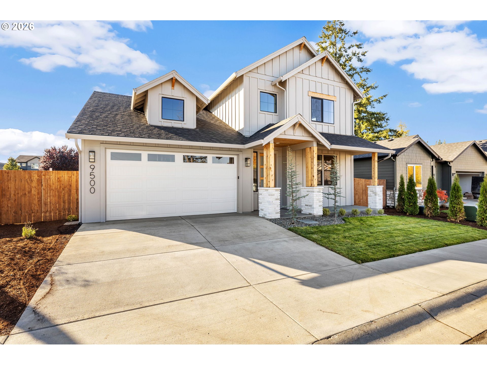 Two-story white house with a covered porch, double garage, and broad concrete driveway.