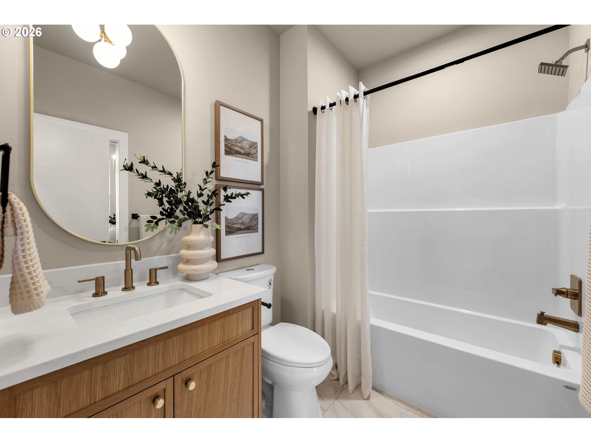 Bathroom with a white tub, wood vanity, brass fixtures, and oval mirror.