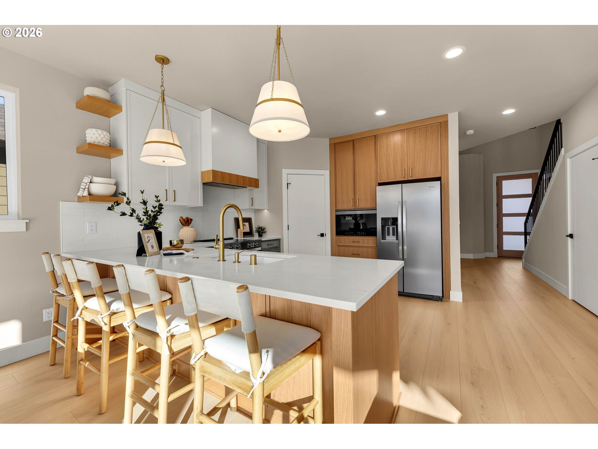 Modern kitchen with a large white island, warm wood cabinetry, and brass pendant lights.
