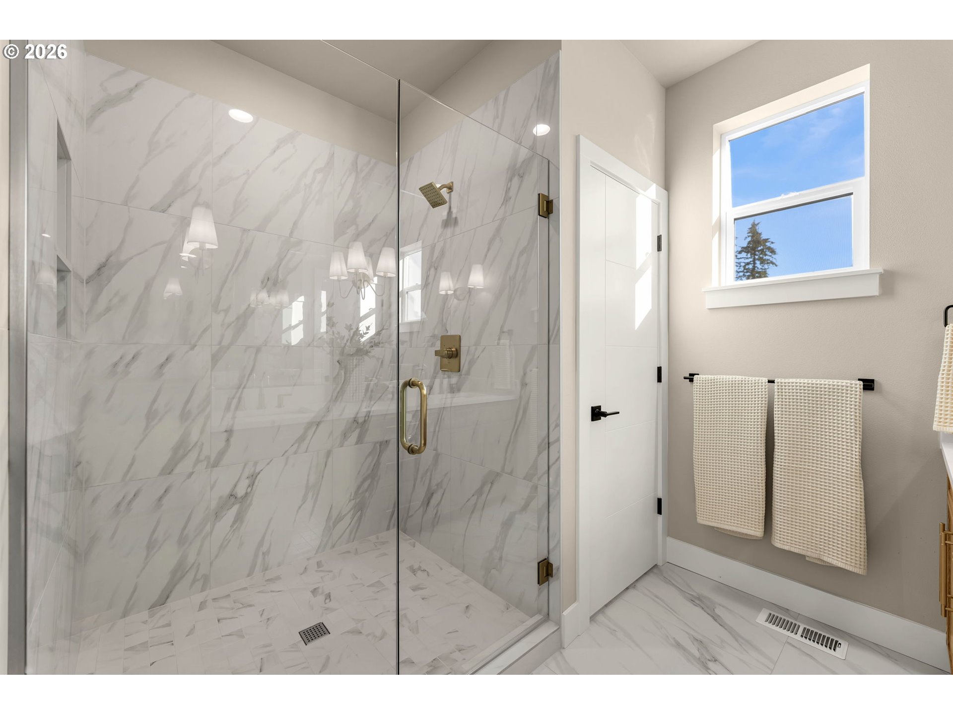 Marble-look walk-in shower with brass fixtures beside a window and towel rack.