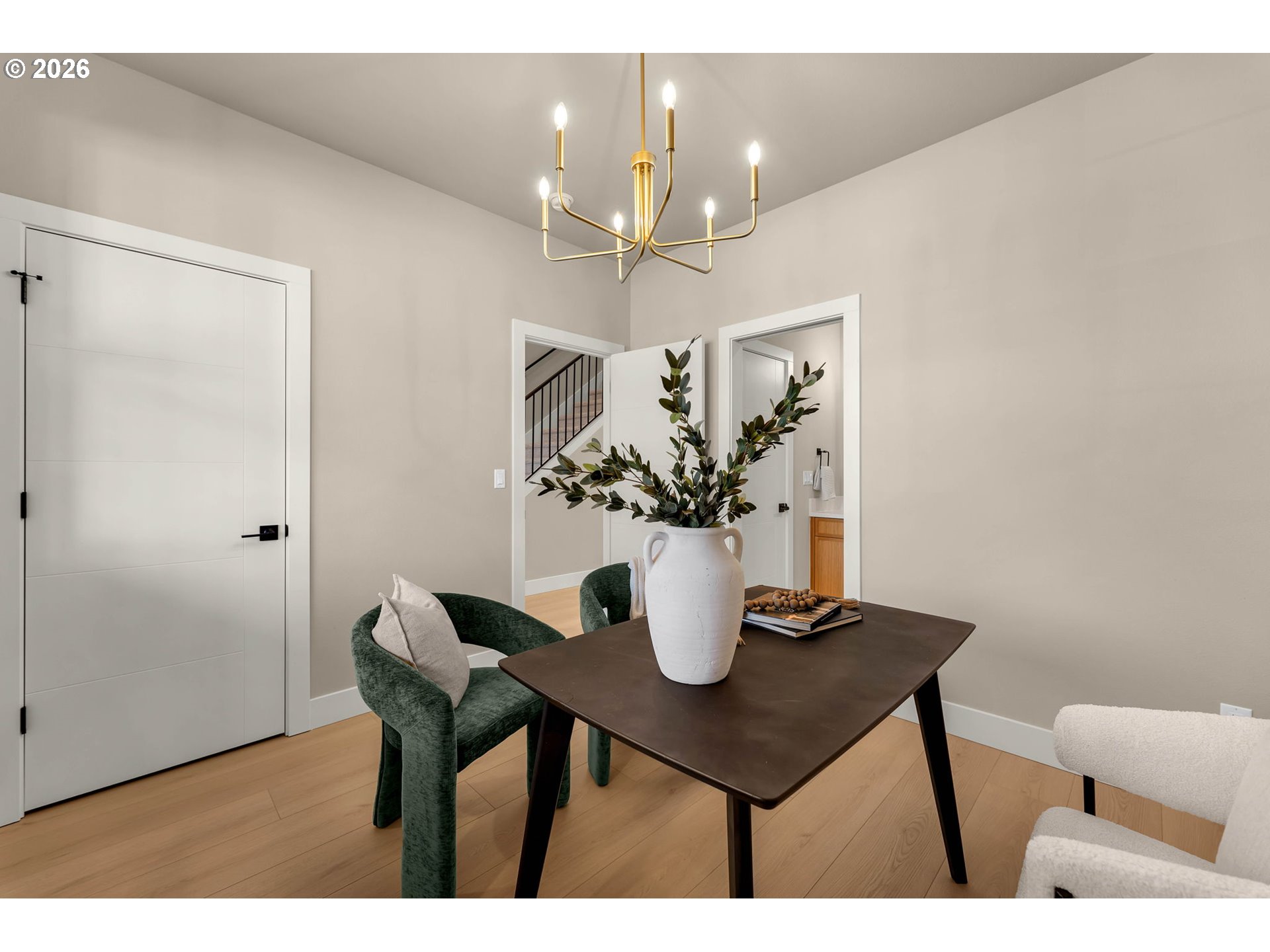 Staged dining area with a dark table, green chairs, and a brass chandelier.