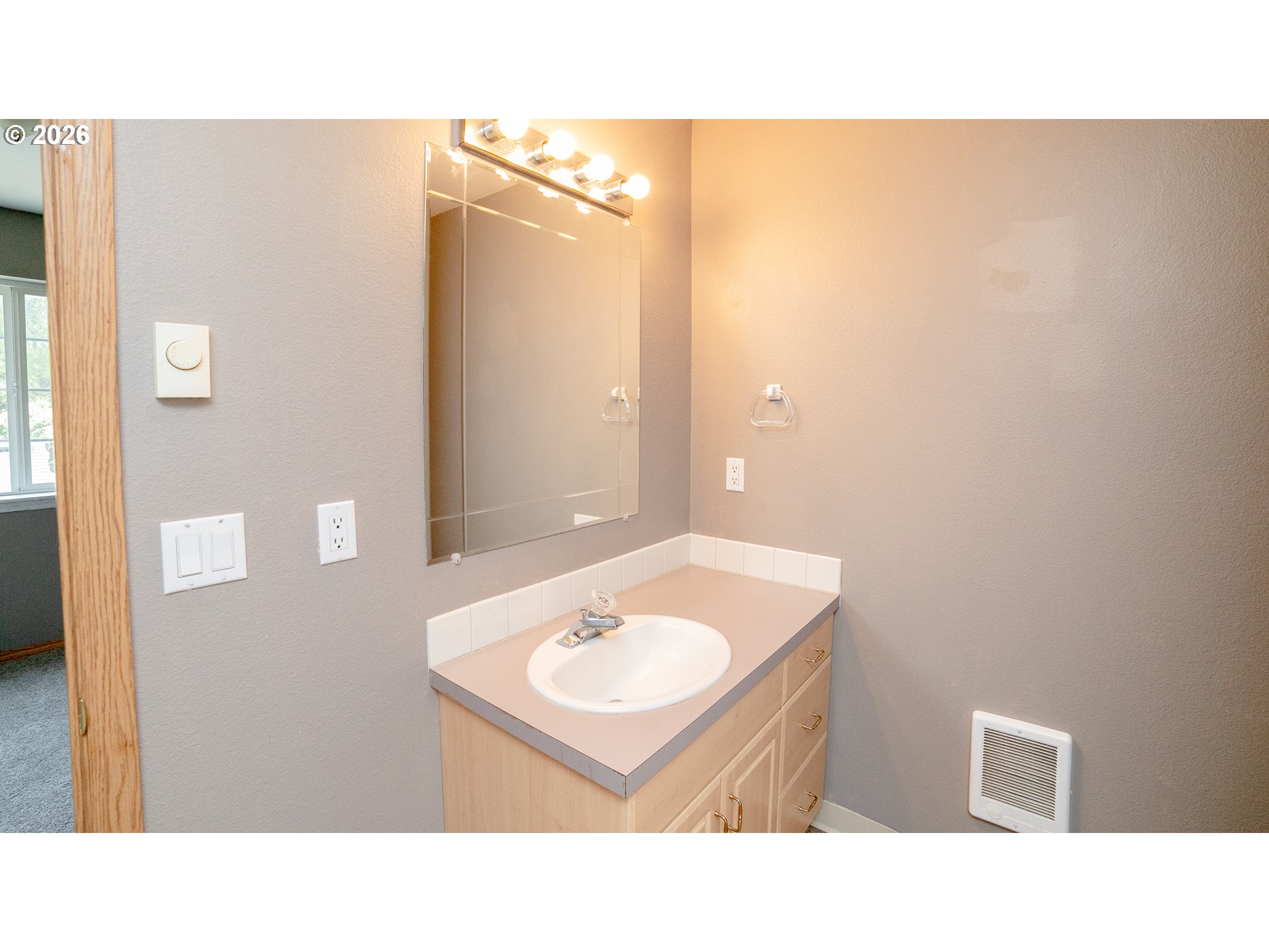 Bathroom vanity with an oval sink, light wood cabinets, and a large mirror with vanity lights.