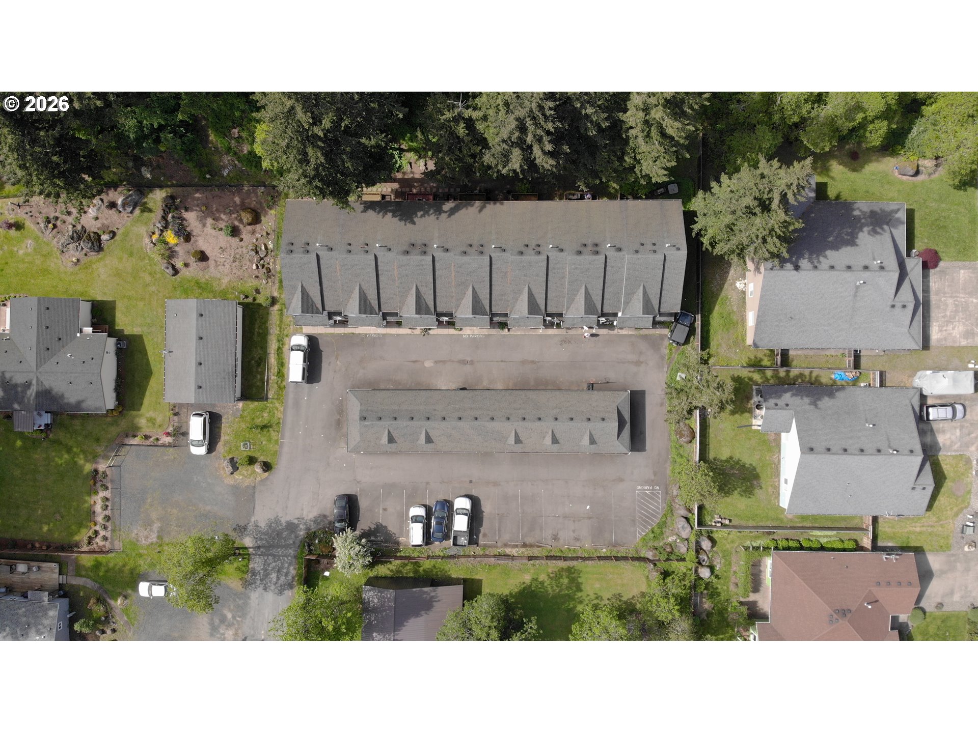 Aerial view of multi-unit buildings around a parking lot, with parked cars and mature trees.