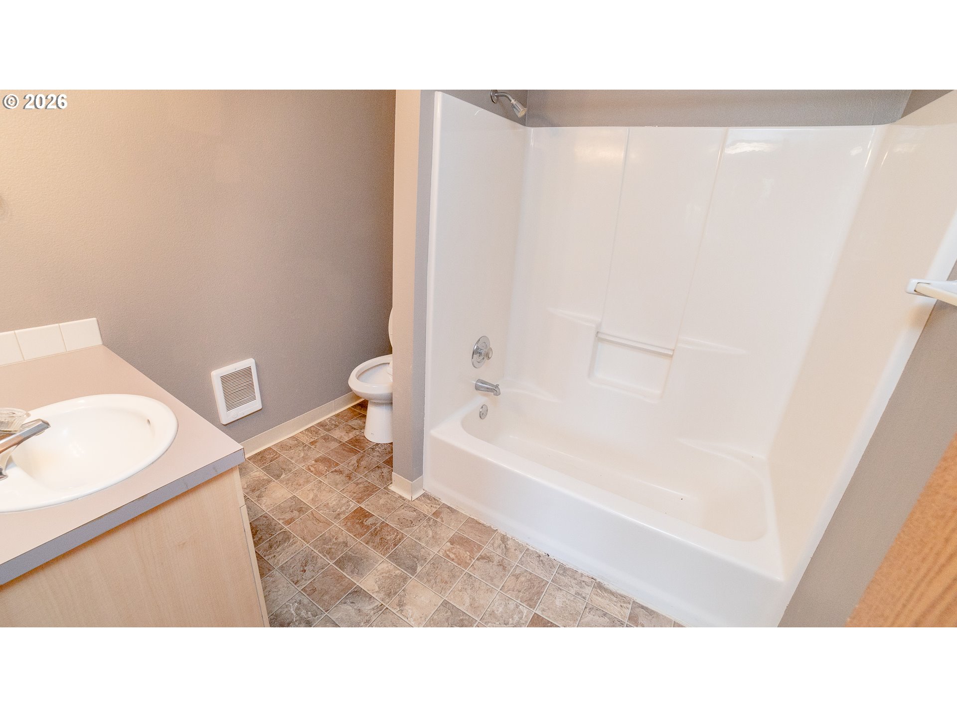 Bathroom with a white tub and shower, vanity sink, toilet, and brown tile floor.