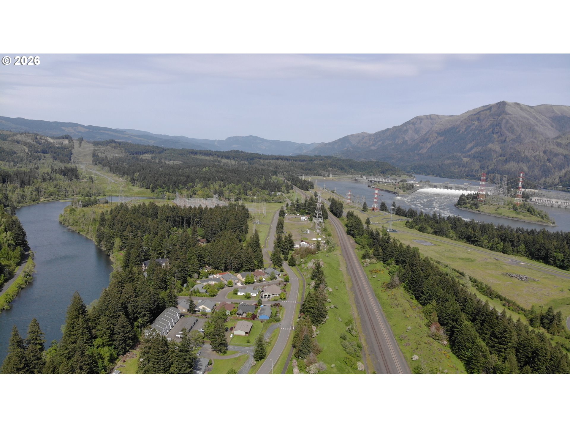 Aerial view of a riverside neighborhood, hydroelectric dam, and forested mountains.