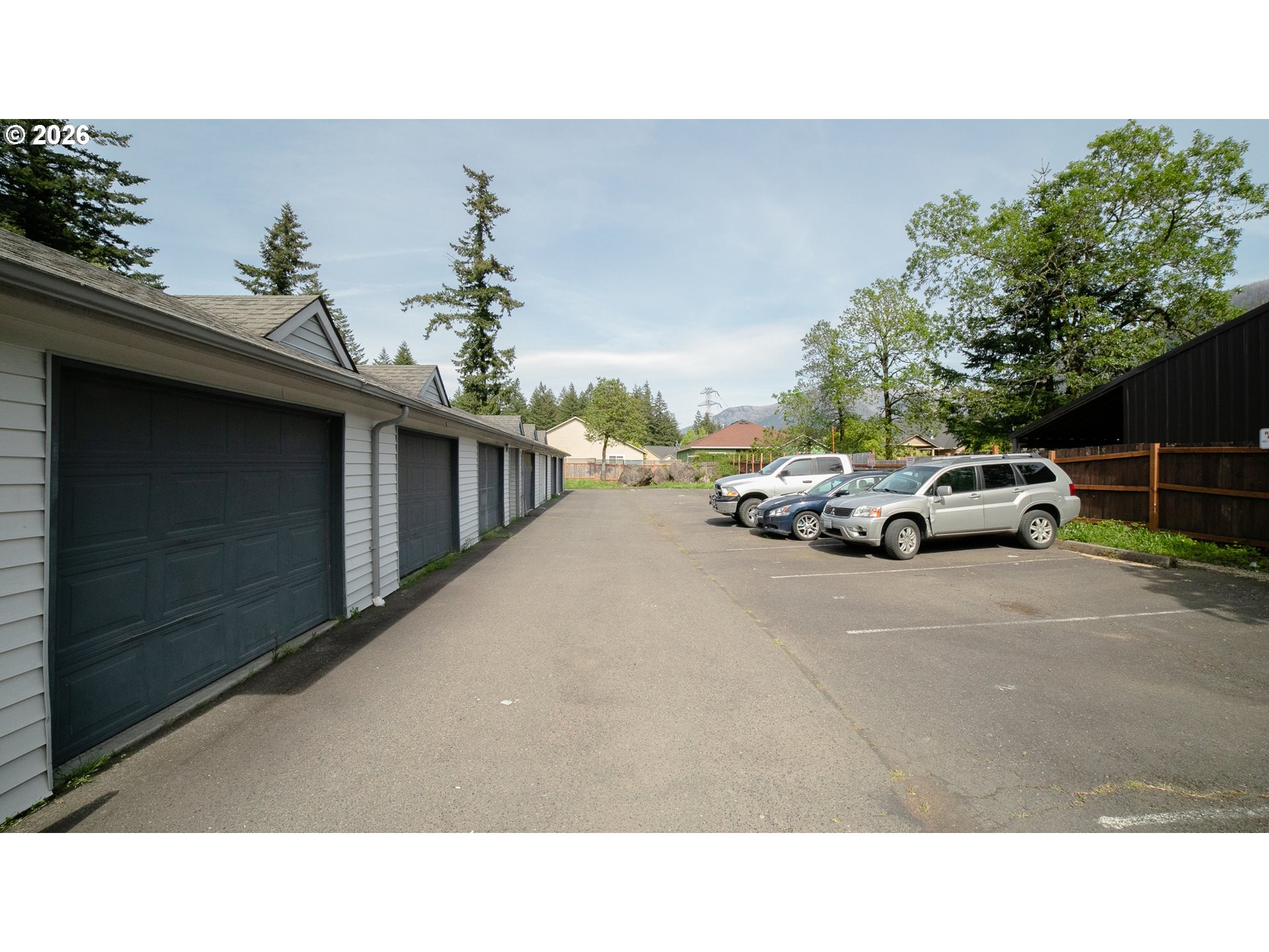 Parking area beside a row of garages, with several cars parked along the fence.