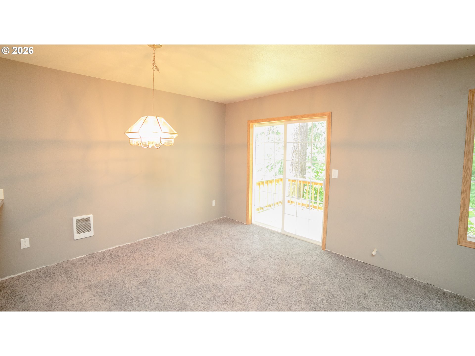 Empty carpeted room with a chandelier and sliding glass door to a deck.