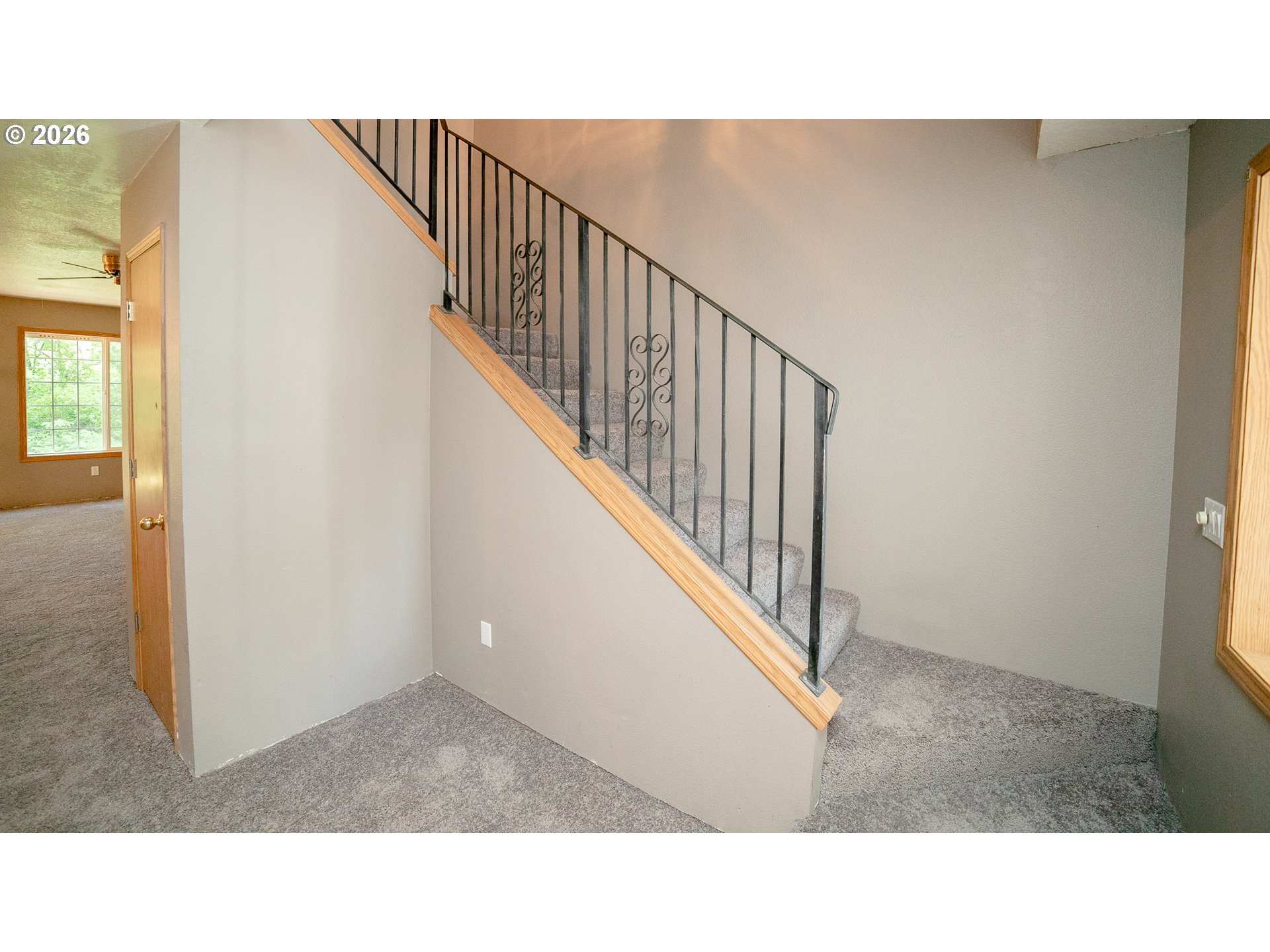 Carpeted staircase with decorative black railing and light wood handrail in an empty foyer.