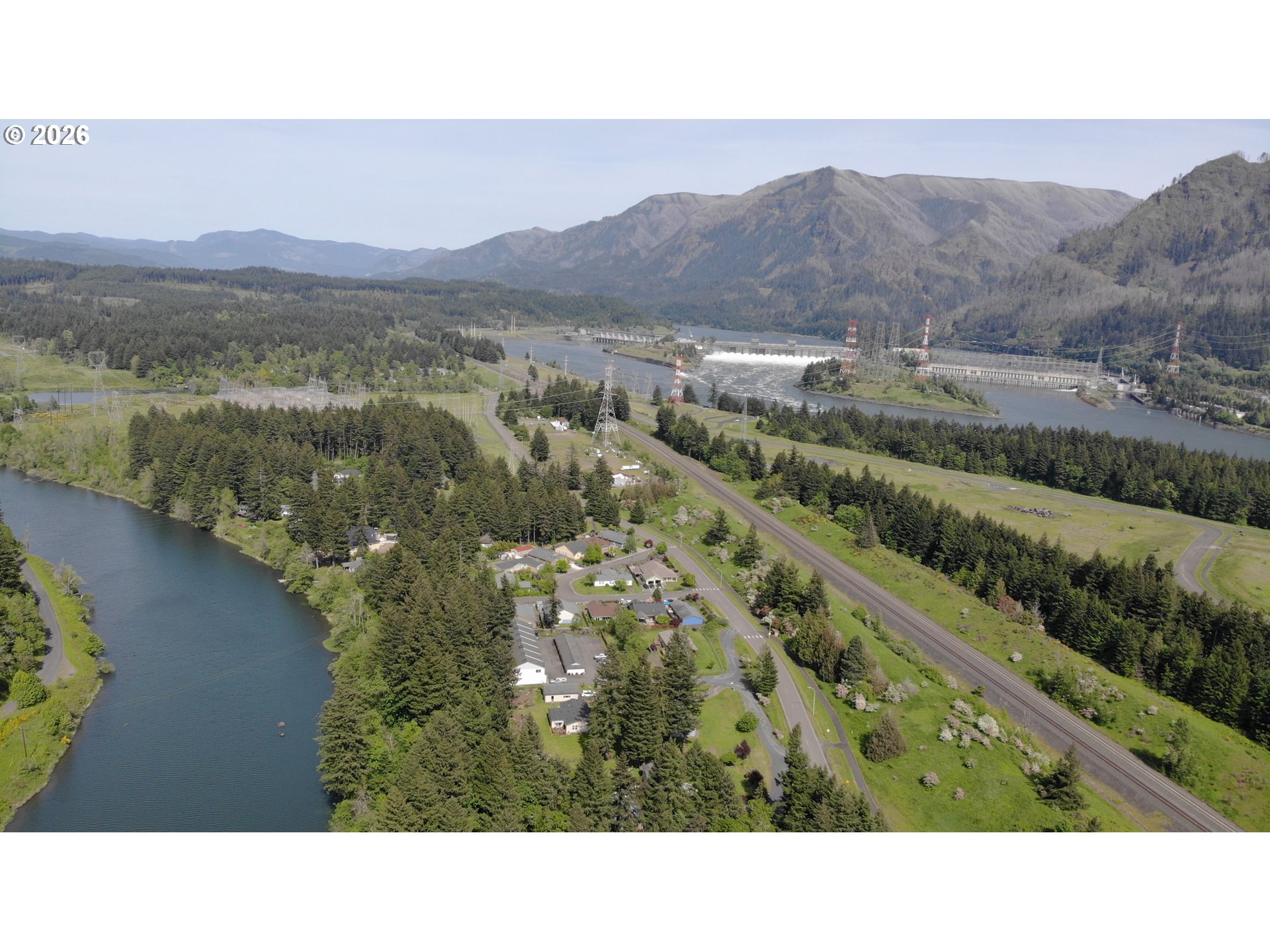 Aerial view of a riverside neighborhood, forested mountains, and a hydroelectric dam.