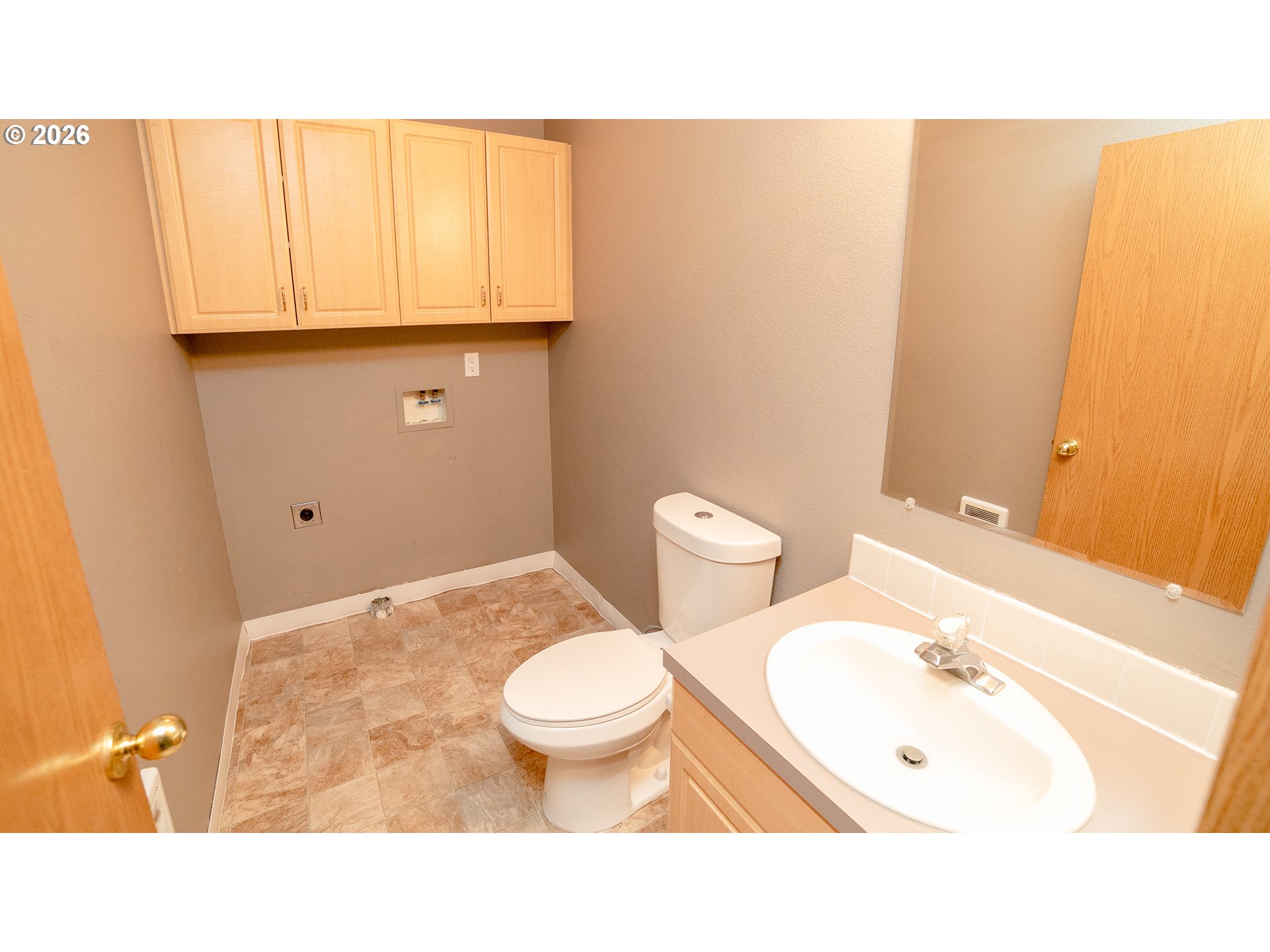 Bathroom with a white toilet, sink vanity, mirrored wall, and washer and dryer hookups.
