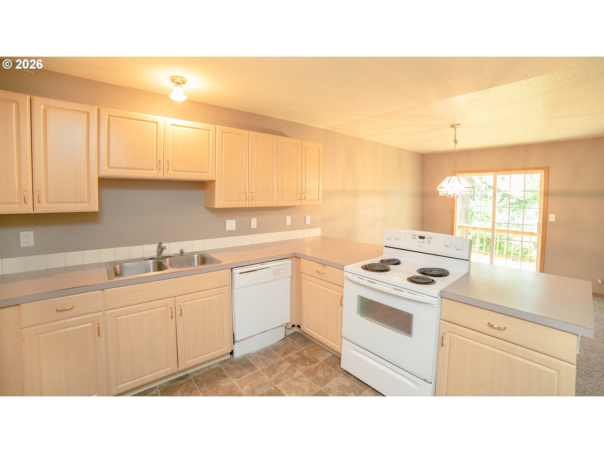 Kitchen with light wood cabinets, gray countertops, and a glass door to the deck.