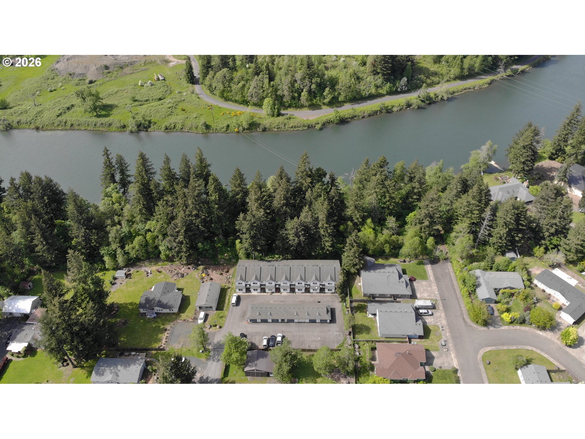 Aerial view of riverside homes and a multi-unit building among dense trees.