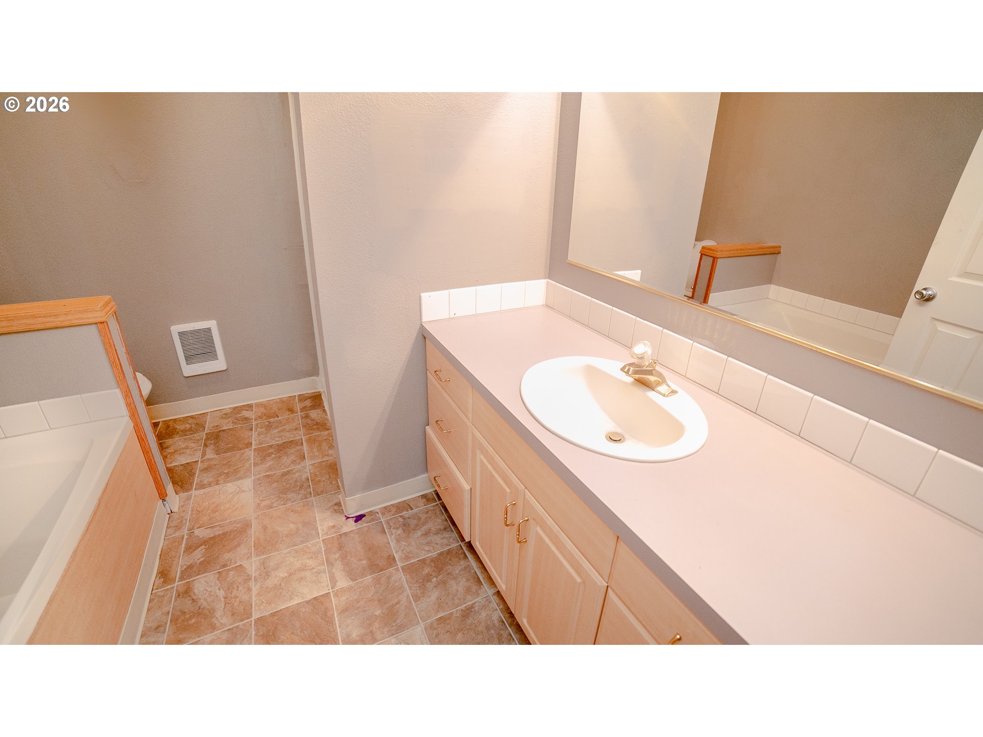 Bathroom with a long wood vanity, oval sink, large mirror, and partially visible bathtub.